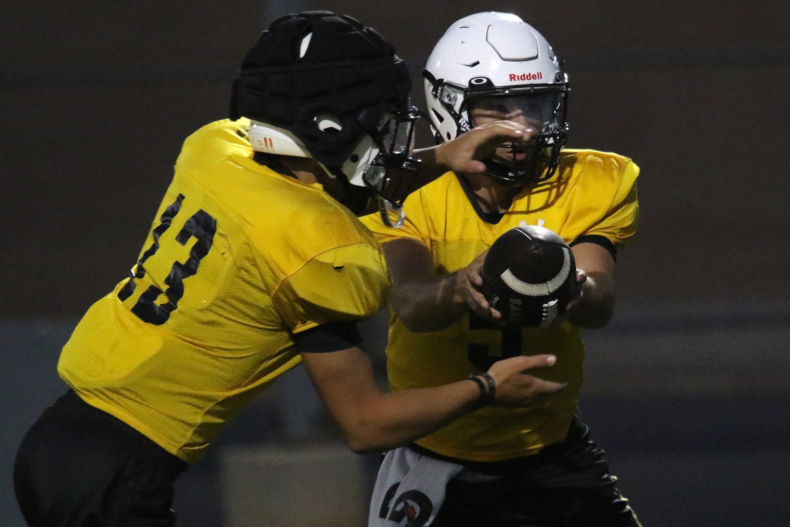 Two football players in yellow jerseys collide; one holds a ball while protecting it from a tackle, wearing white helmet.