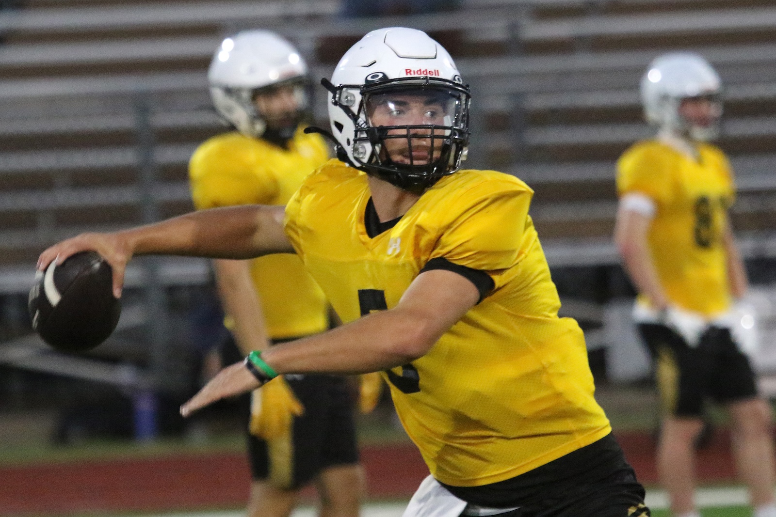 Quarterback in a yellow jersey throwing a football on a football field during practice or game.