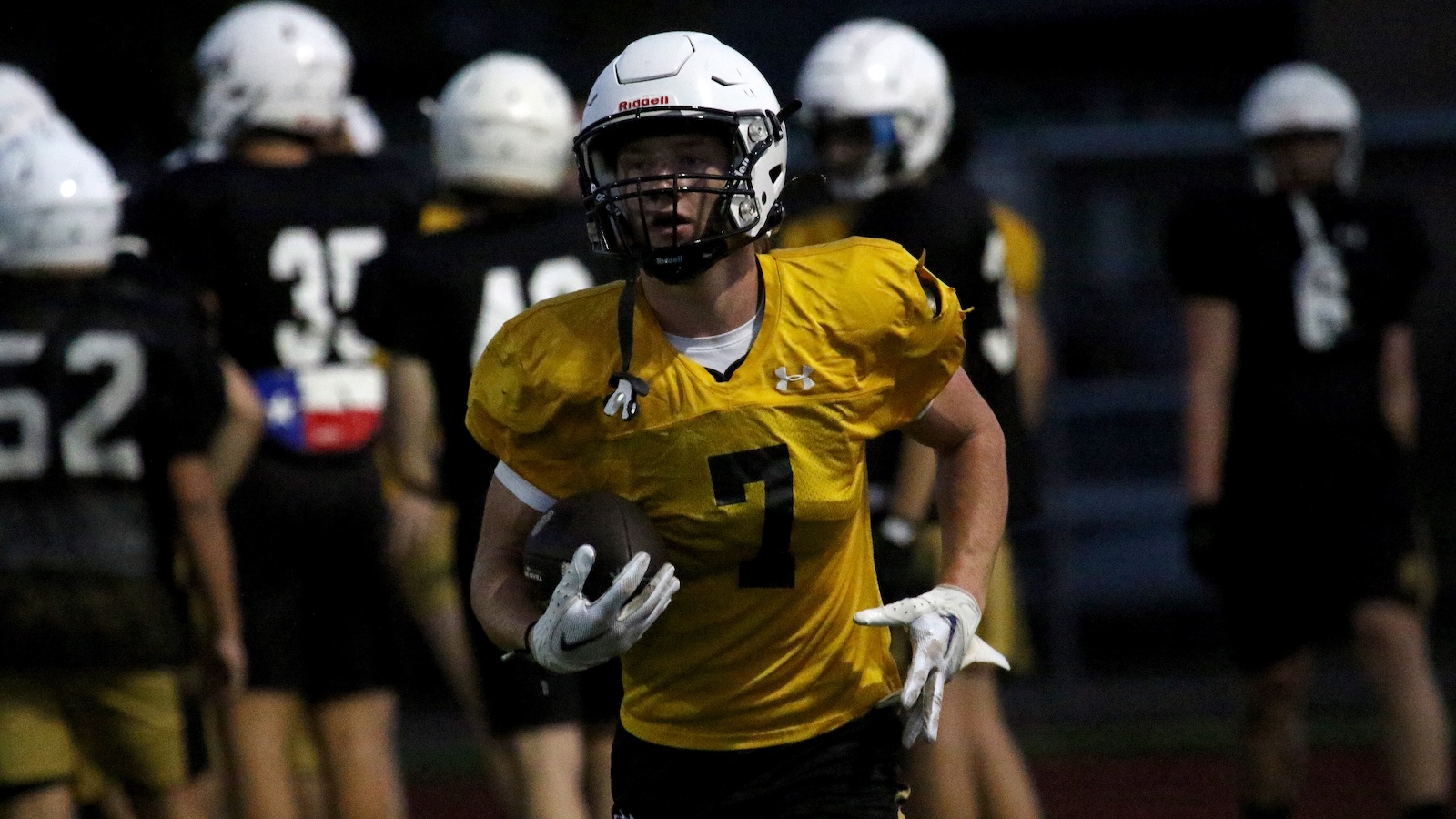 Football player in a gold jersey with number 7 running with the ball during a game.