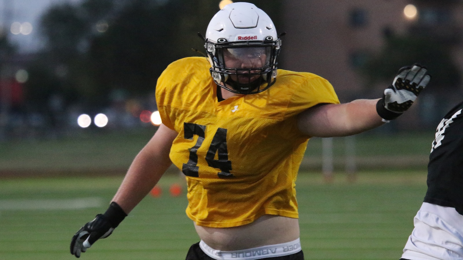 Football player in a yellow jersey #34 extends an arm during a play on a grassy field at dusk/evening.
