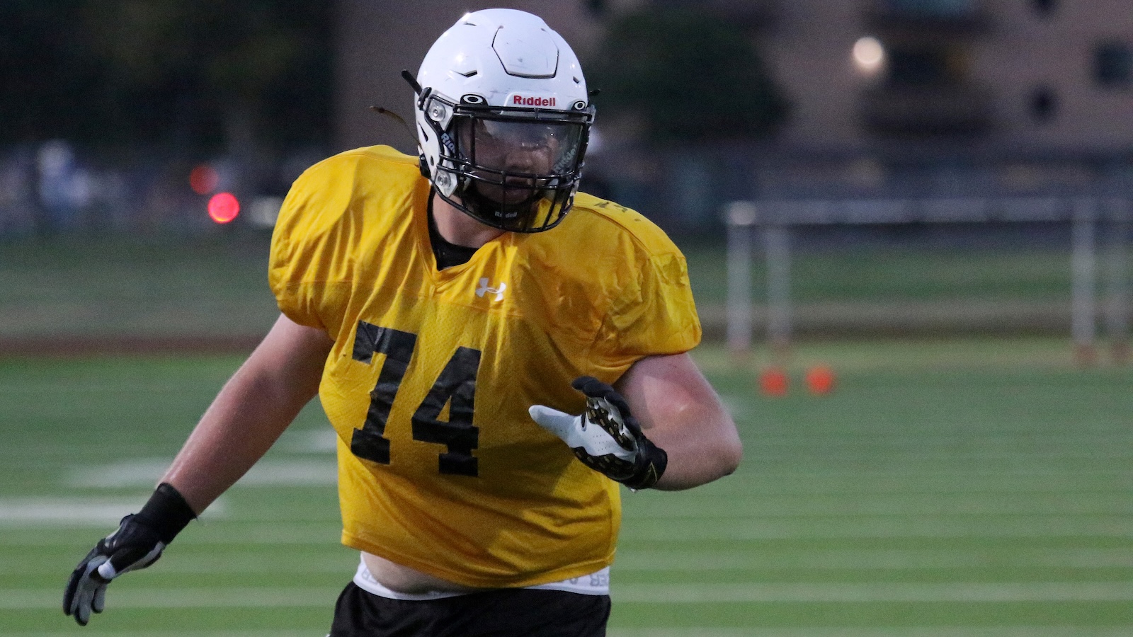 American football player in a yellow jersey #14 runs on a green field, wearing a white helmet and black gloves.