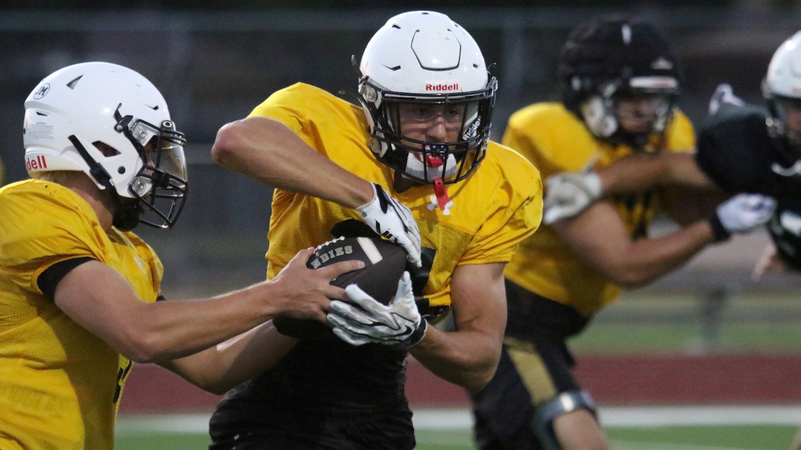 Yellow-jersey football players collide as the ball carrier protects the ball while a teammate reaches in during a tackle.
