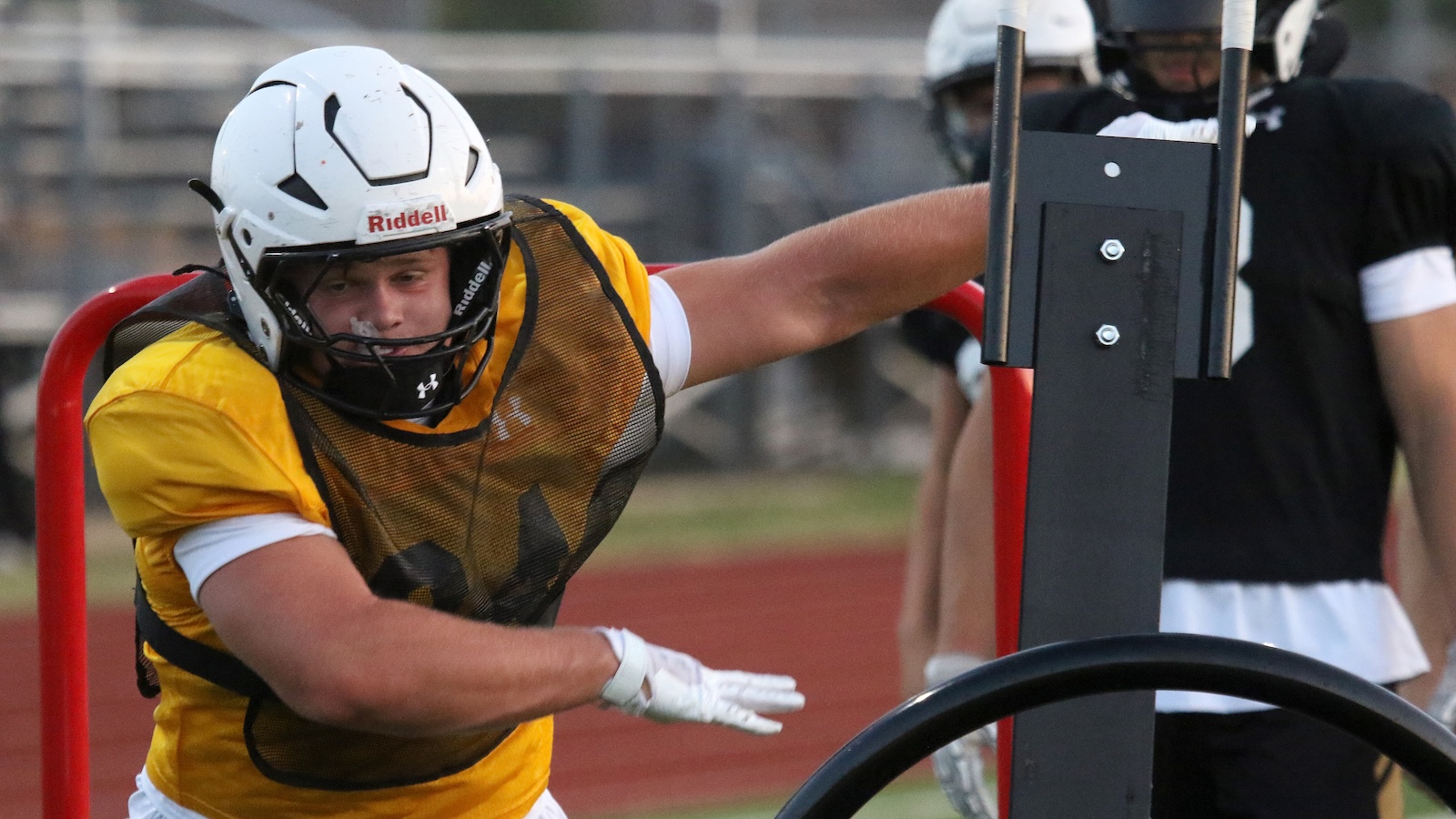 American football practice: lineman in a yellow jersey pushes against a blocking sled during drills