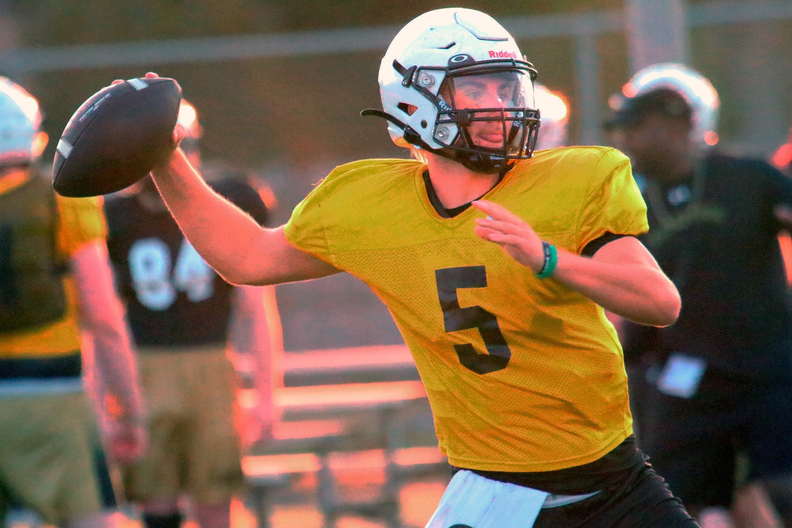 Quarterback in a yellow jersey throws a pass during a game or practice, wearing a white helmet with a facemask.