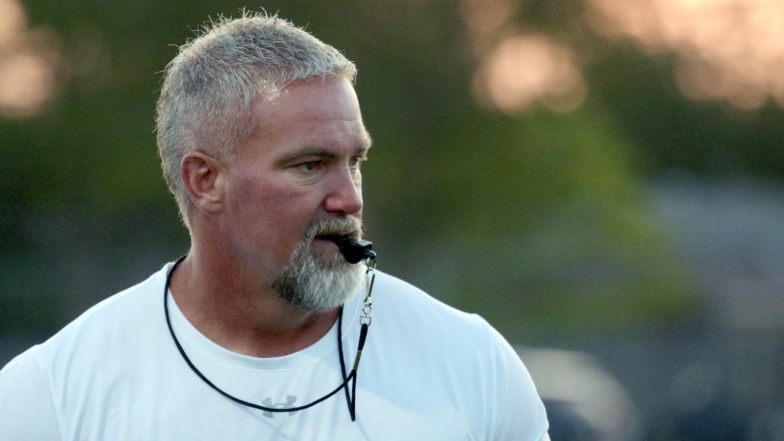 Man with short gray hair and a goatee wearing a headset microphone outdoors, looking to the right.