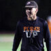 Dumas - Grow Your Own - Parker Dunnam | Press Pass Sports Man wearing a black long-sleeve shirt with orange 'FORKS' lettering stands on a dimly lit sports field at night, smiling slightly. Cap visible on head.