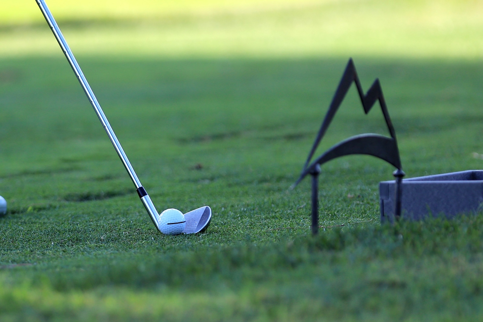 Golfer's club about to strike a white golf ball perched on a tee on a well-manicured green.