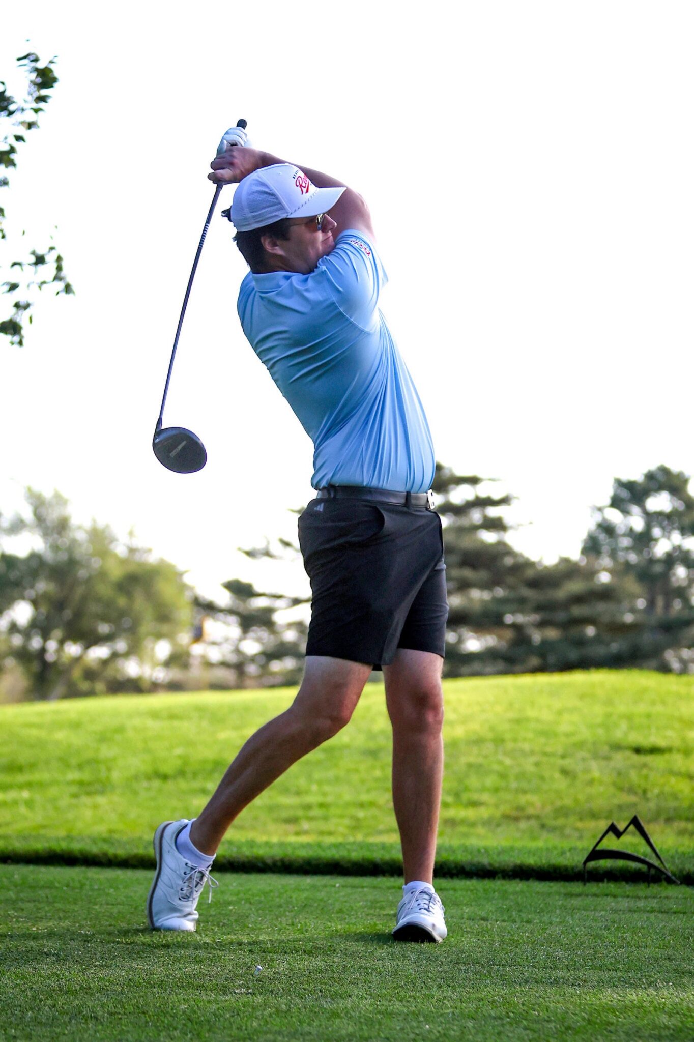 20260813-CoorsTOC-Day1-023 | Press Pass Sports Male golfer in a light blue polo swinging a driver on a green golf course, wearing a white cap and sunglasses with a backdrop of trees.