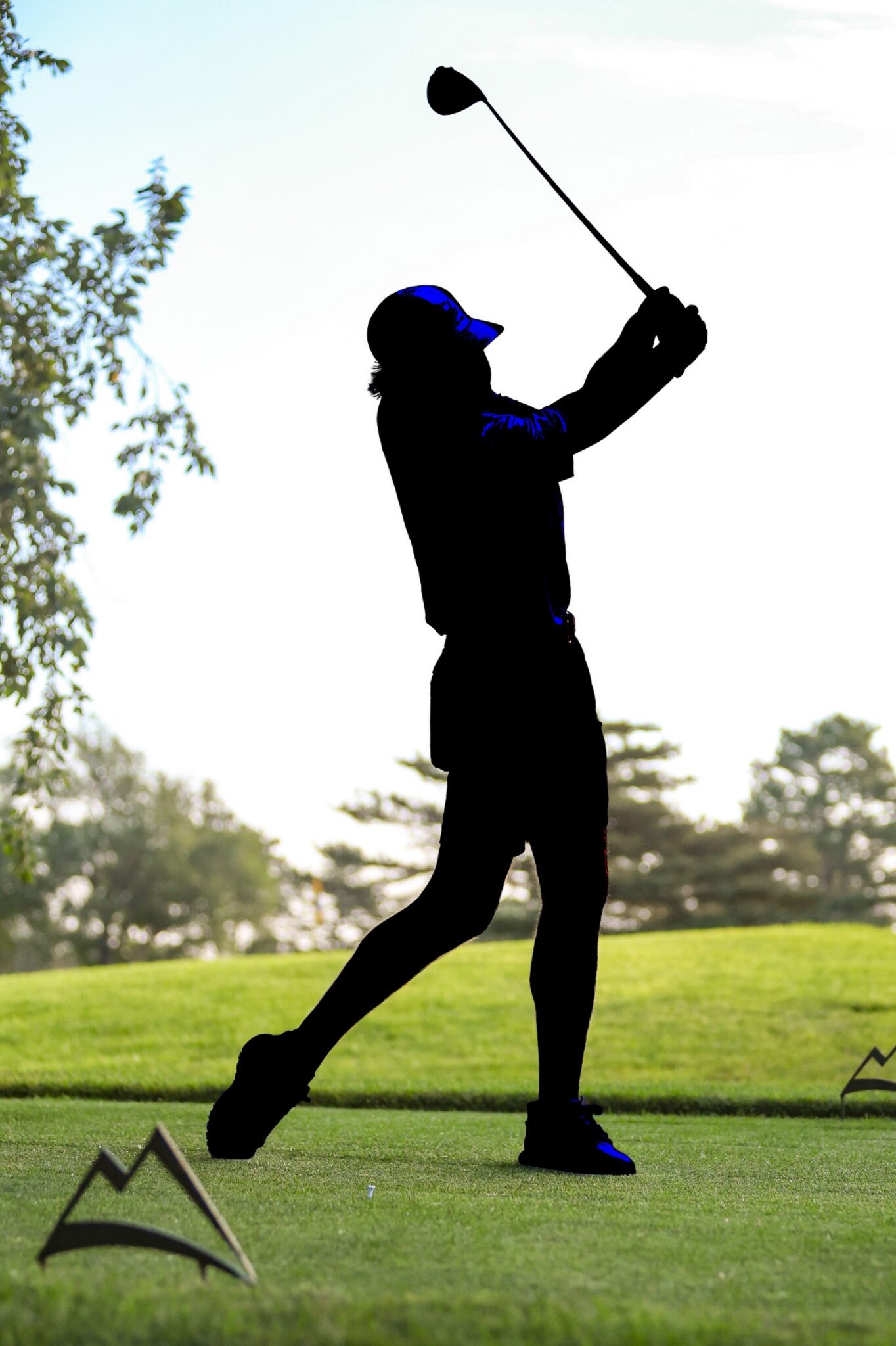 20260813-CoorsTOC-Day1-025 | Press Pass Sports Silhouette of a golfer mid-swing on a sunny golf course, with trees and green fairway in the background.