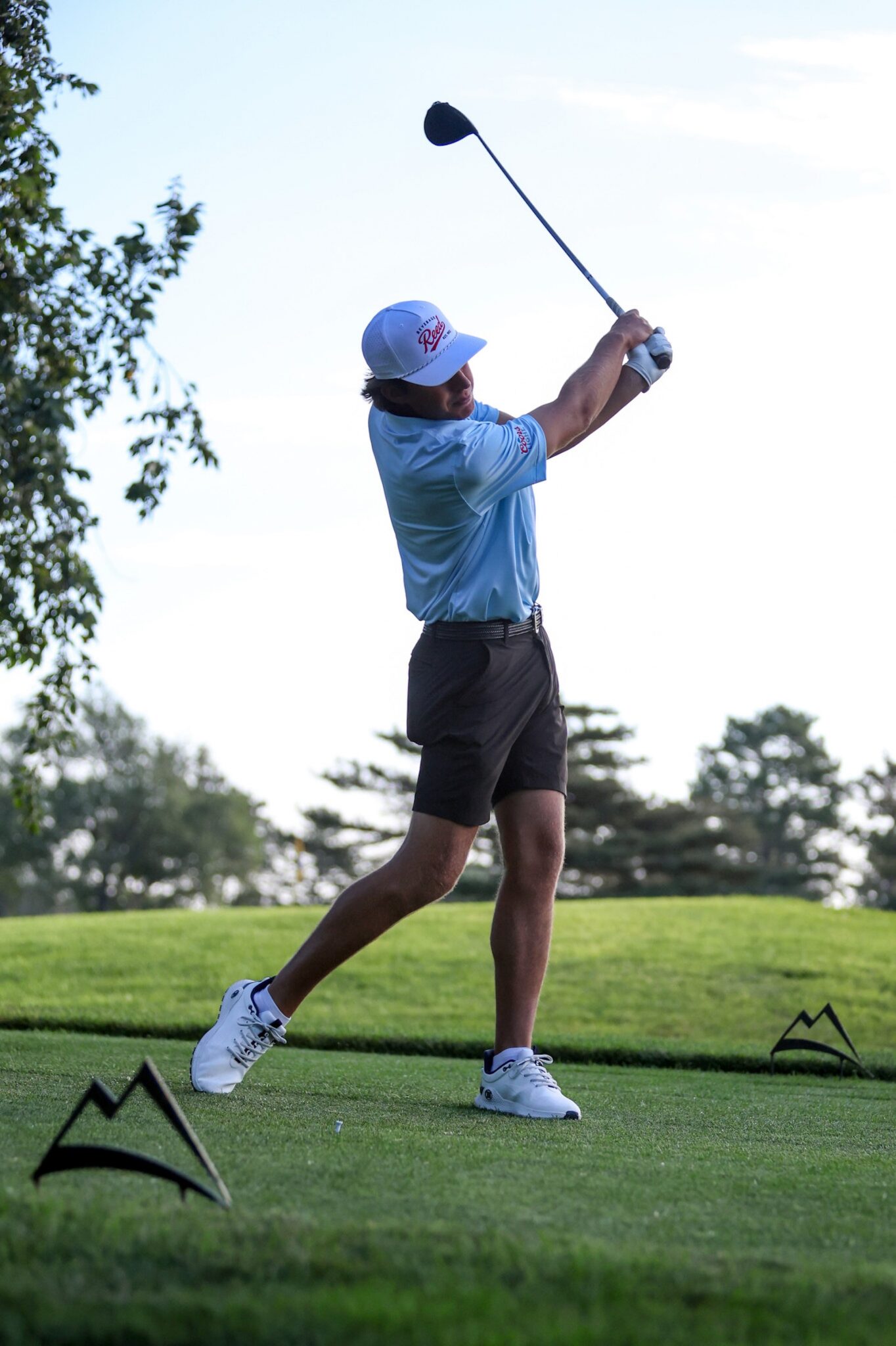 20260813-CoorsTOC-Day1-026 | Press Pass Sports Golfer in a light blue shirt and white cap mid-swing on a sunny golf course, with tee markers in the foreground.