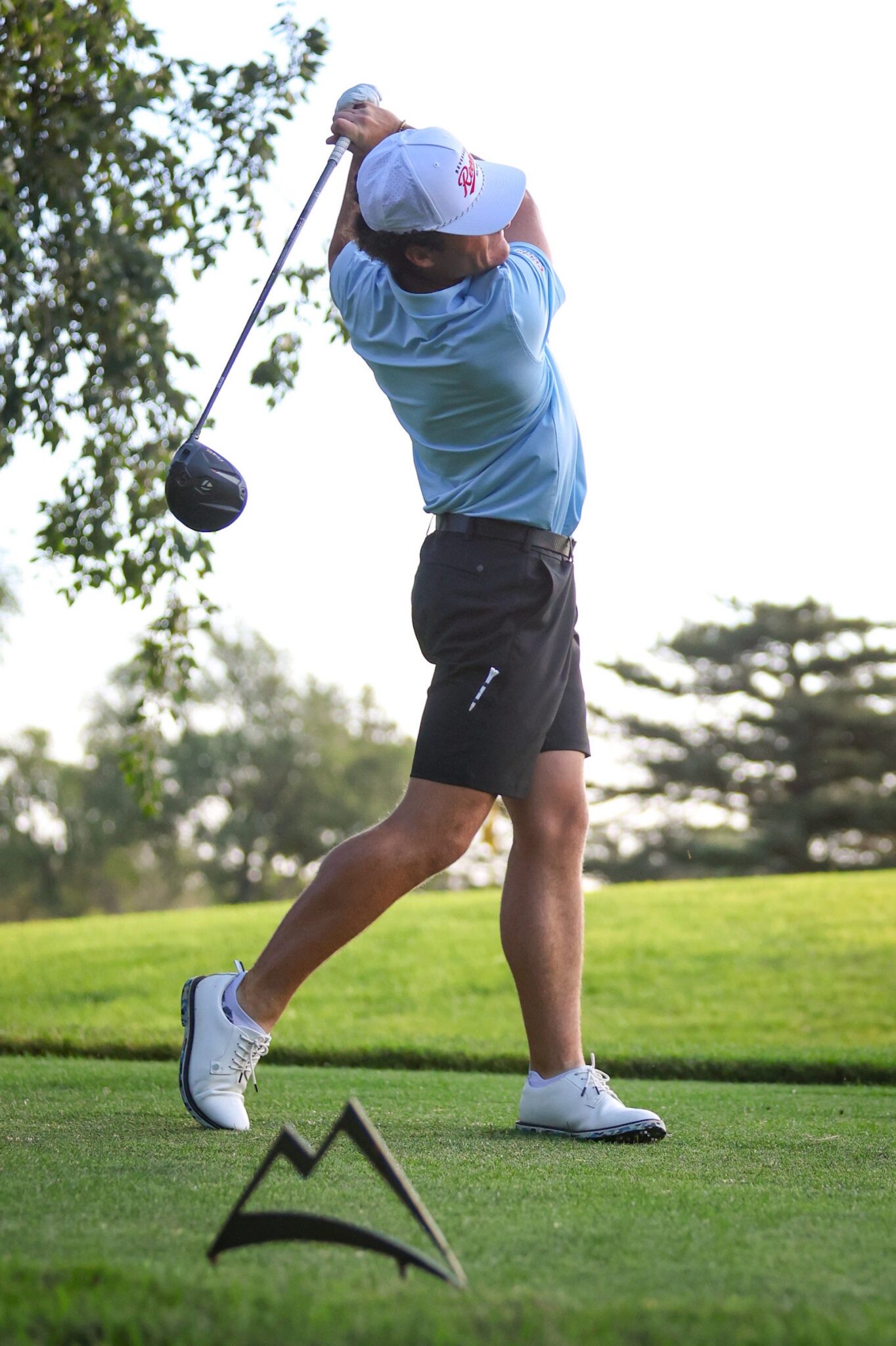 20260813-CoorsTOC-Day1-027 | Press Pass Sports Golfer in light blue shirt and cap mid-swing on a green golf course, with tee markers in the foreground