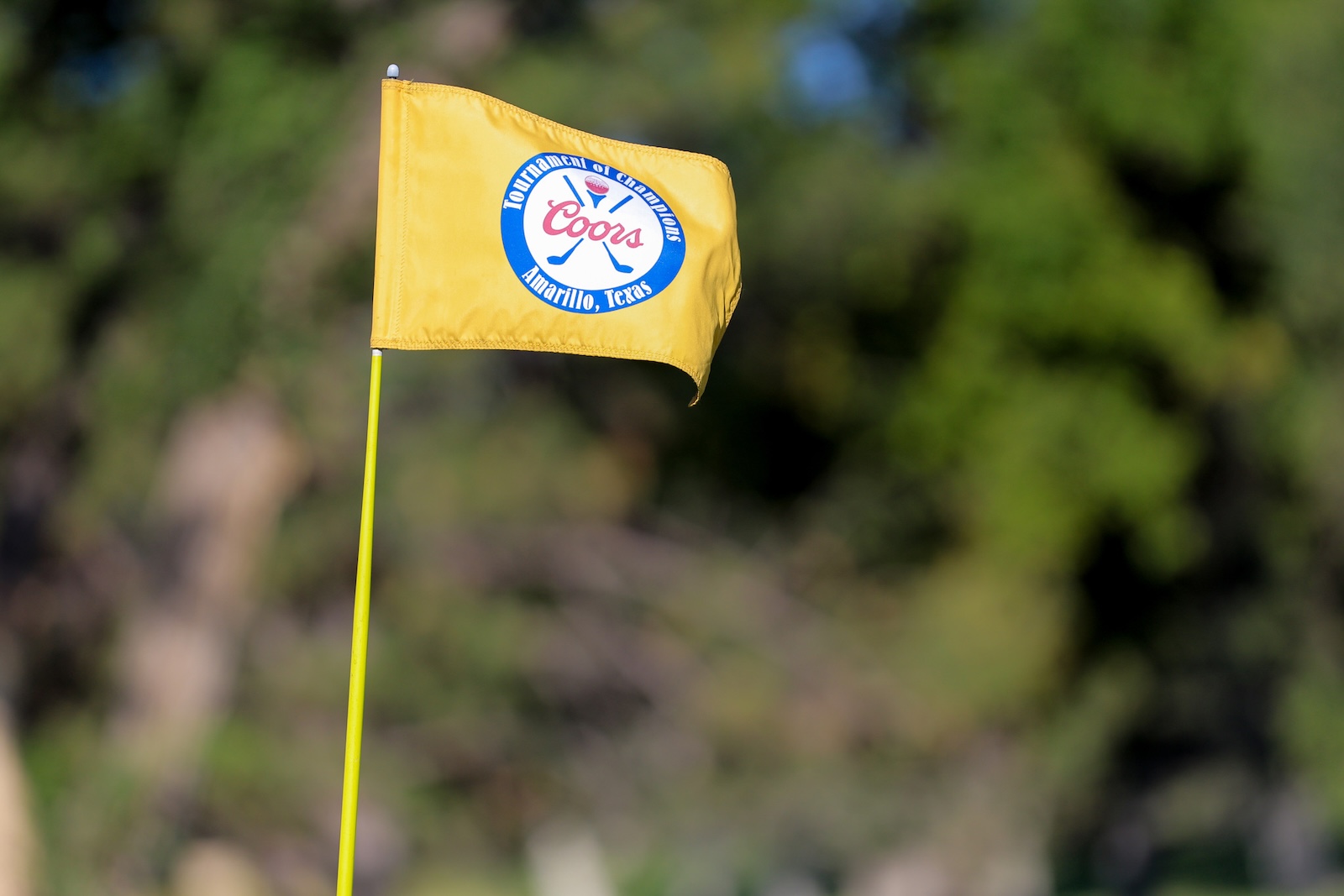 Yellow flag on a golf hole flagstick with a Coors logo and'Tournament of Champions' text on a blue circle, Amarillo, Texas.