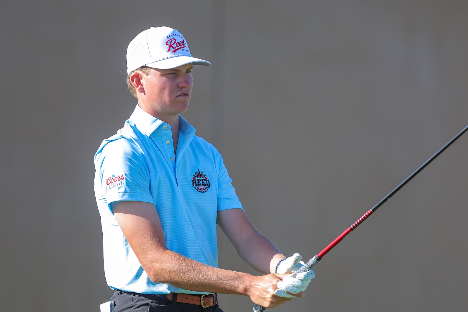 Young man golfer in a light blue polo and white cap preparing to swing with a golf club in his hands.