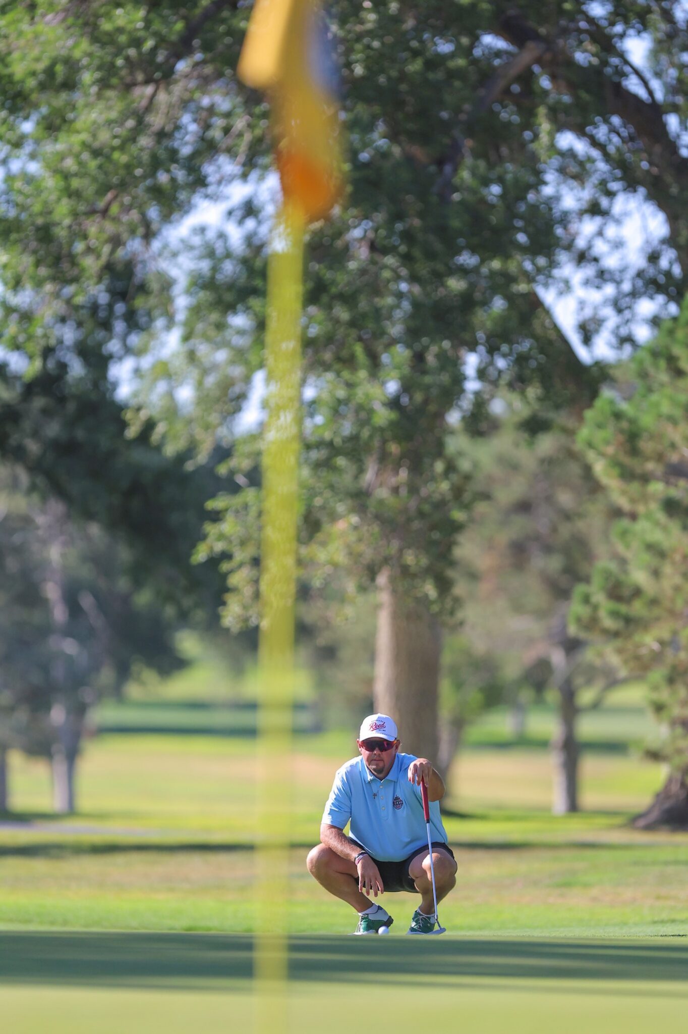 20260813-CoorsTOC-Day1-058 | Press Pass Sports Golfer crouching on the putting green, lining up a putt on a sunny day.