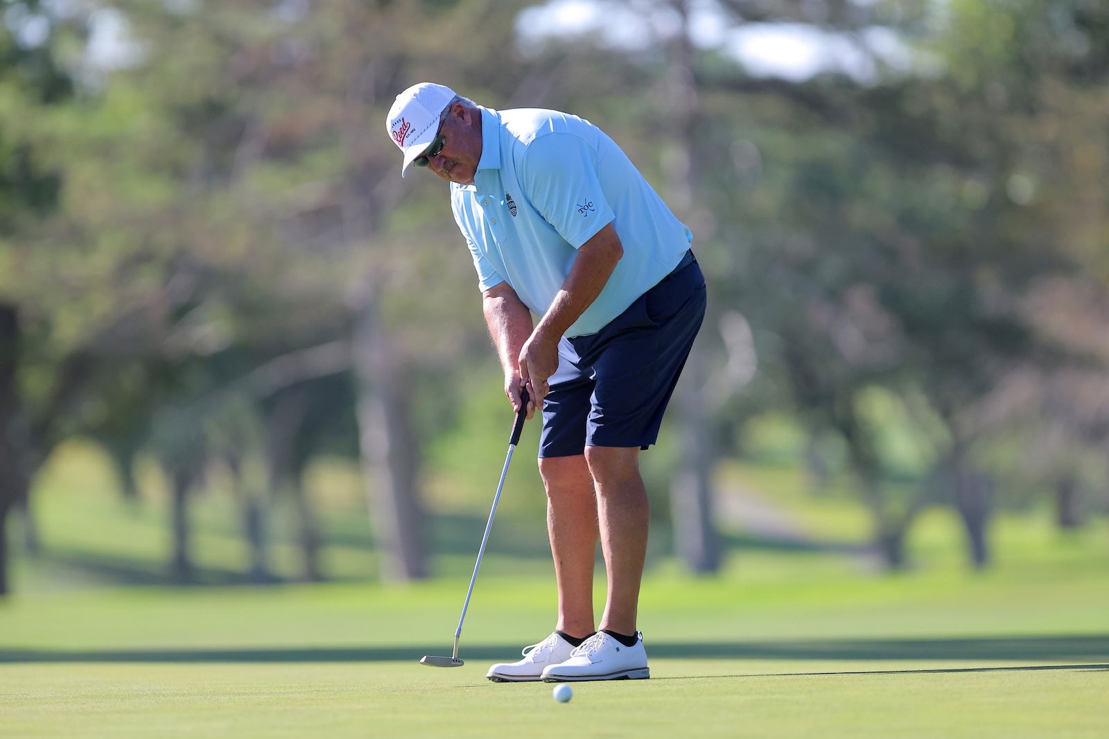 Golfer in a light blue polo and white cap lining up a putt on a green golf course.