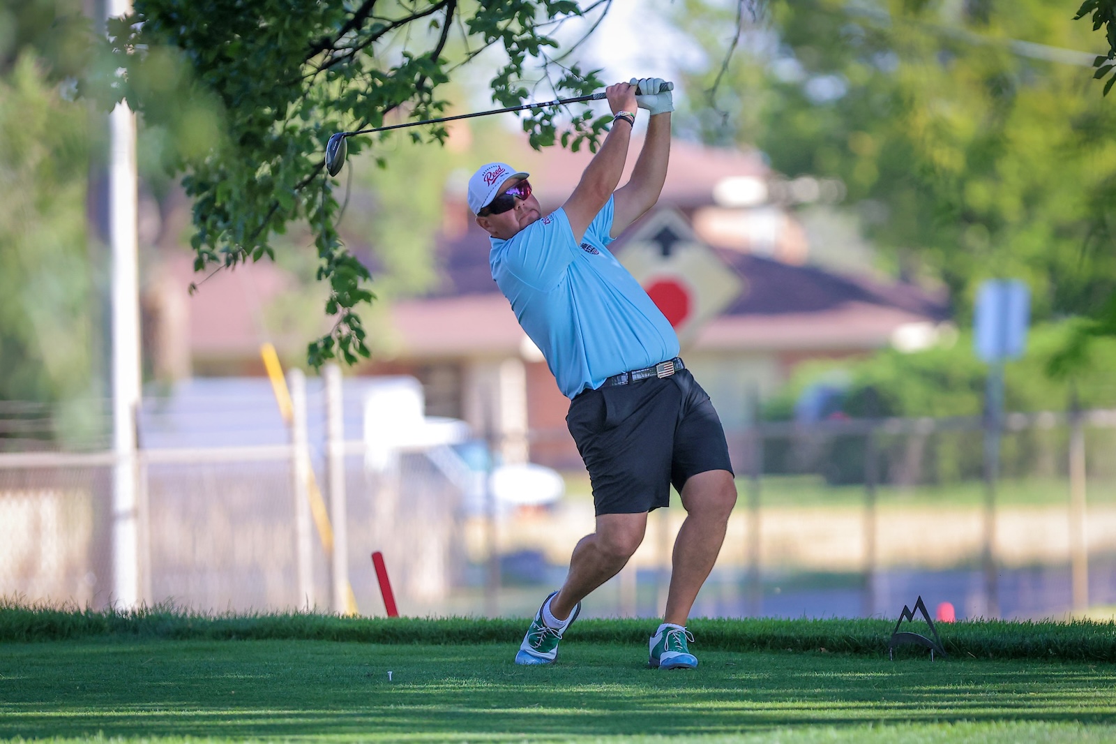 Golfer in a blue shirt and cap taking a backswing on a sunny golf course.