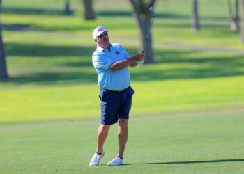 20260813-CoorsTOC-Day1-056 | Press Pass Sports A man in a light blue polo and navy shorts swings a golf club on a lush green course, wearing a white cap and sunglasses.