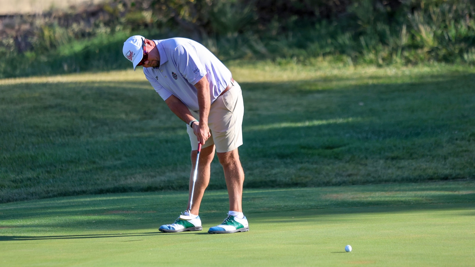 Golfer lining up a putt on a sunny greens, ball a few feet away on the putting surface.