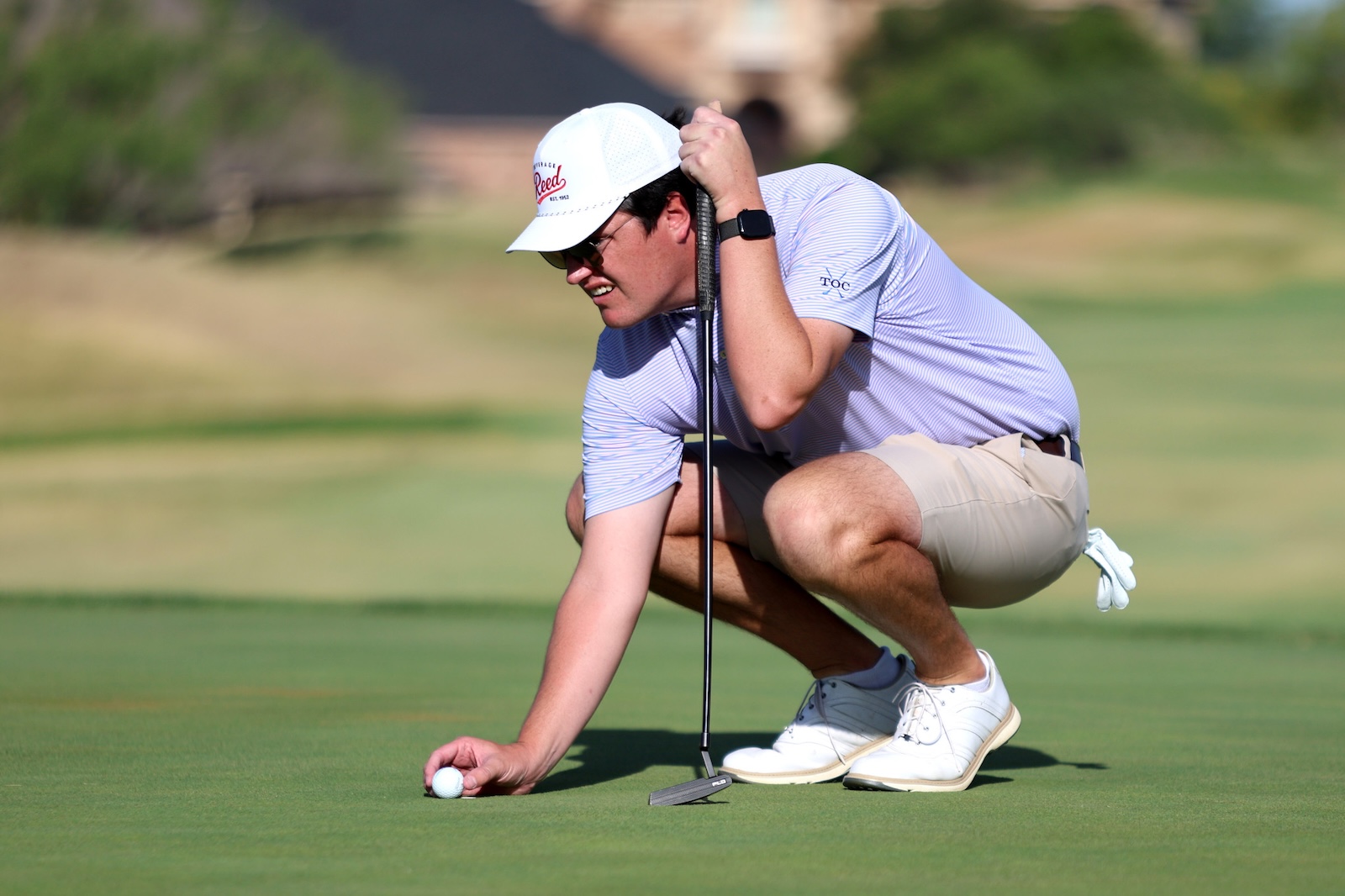 Golfer crouches on the green placing a golf ball with a putter laid down nearby nearby.