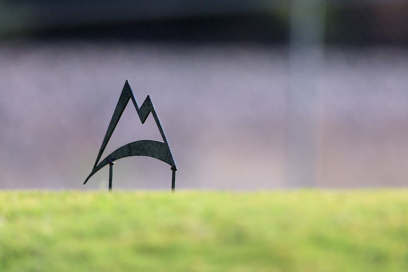 Abstract metal sculpture of stylized mountains on a grassy field with a blurred background.