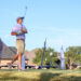 20260814-CoorsTOC-Day2-003 | Press Pass Sports Golfer in a purple polo and beige shorts preparing to swing on an elevated tee during a sunny golf event, with blue sky and flags in the background.