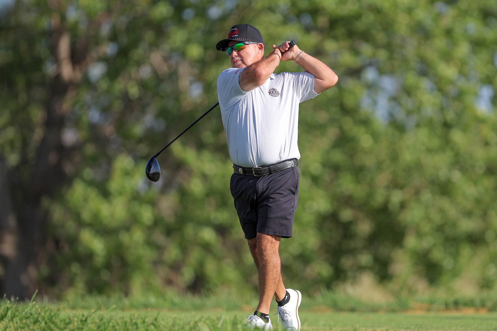Golfer in a light gray polo and black shorts at the moment of a backswing on a sunny golf course.