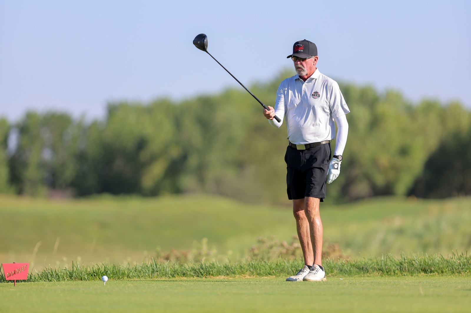 Male golfer on tee, holding a driver and preparing to hit a tee shot on a sunny course.