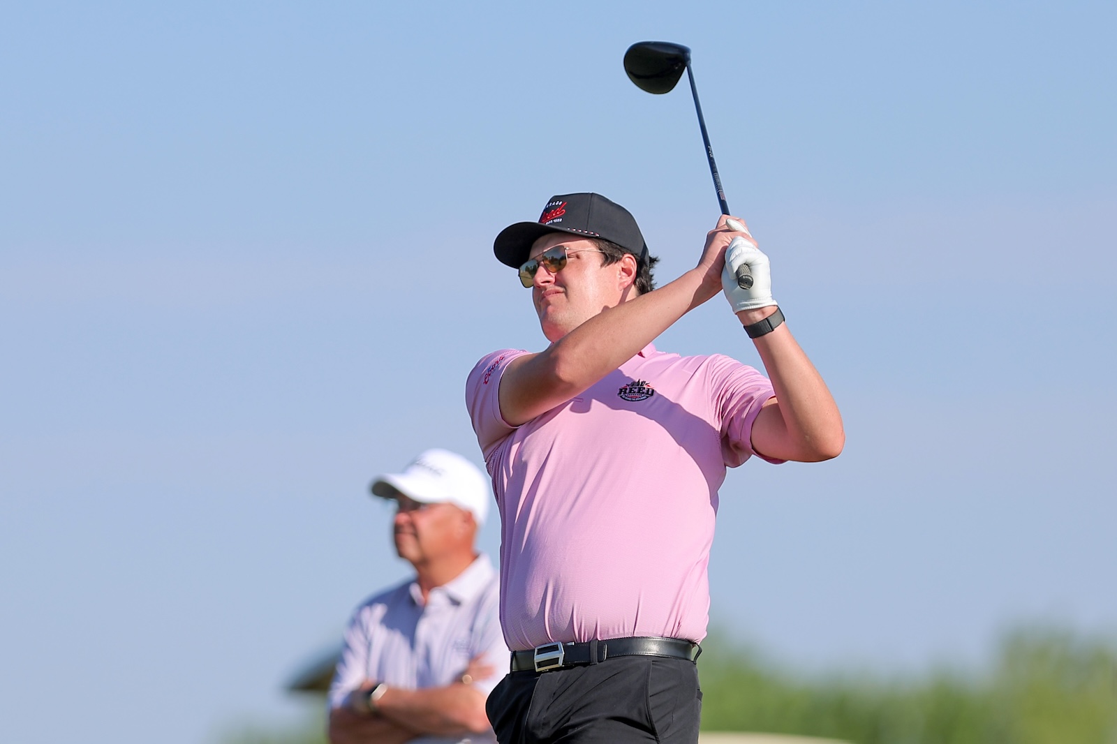 Male golfer in a pink polo swinging a driver on a sunny golf course