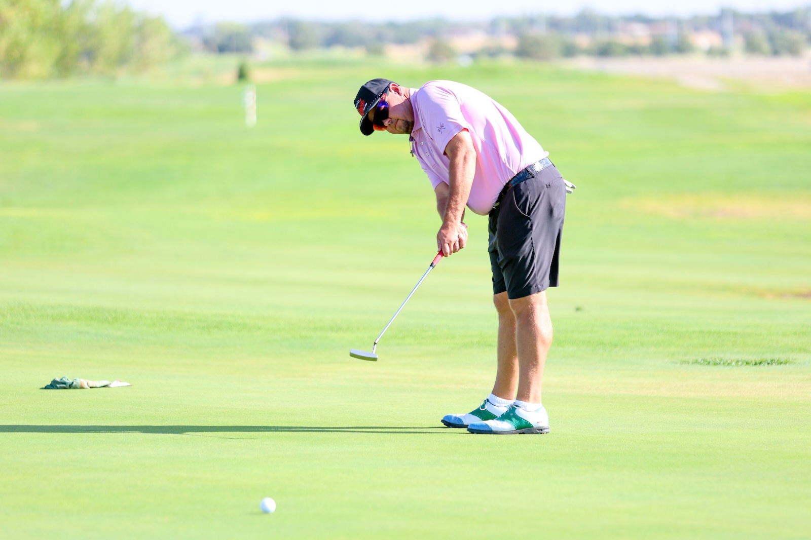 Man in pink polo putting on a golf green, focused on the ball with a putter in hand