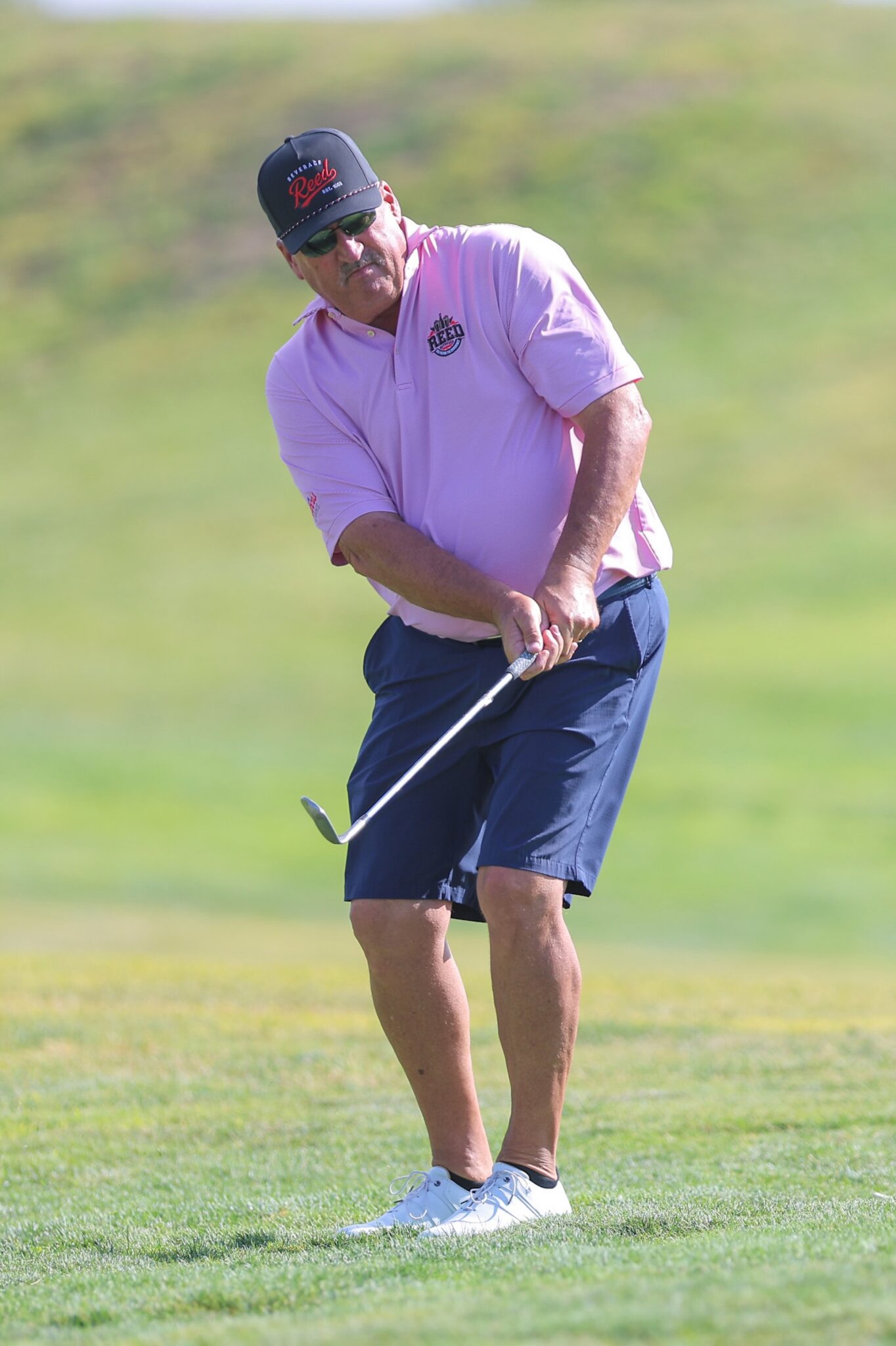 20260815-CoorsTOC-Day3-067 | Press Pass Sports Male golfer in a pink polo and navy shorts mid-swing on a sunny golf course with a green background.
