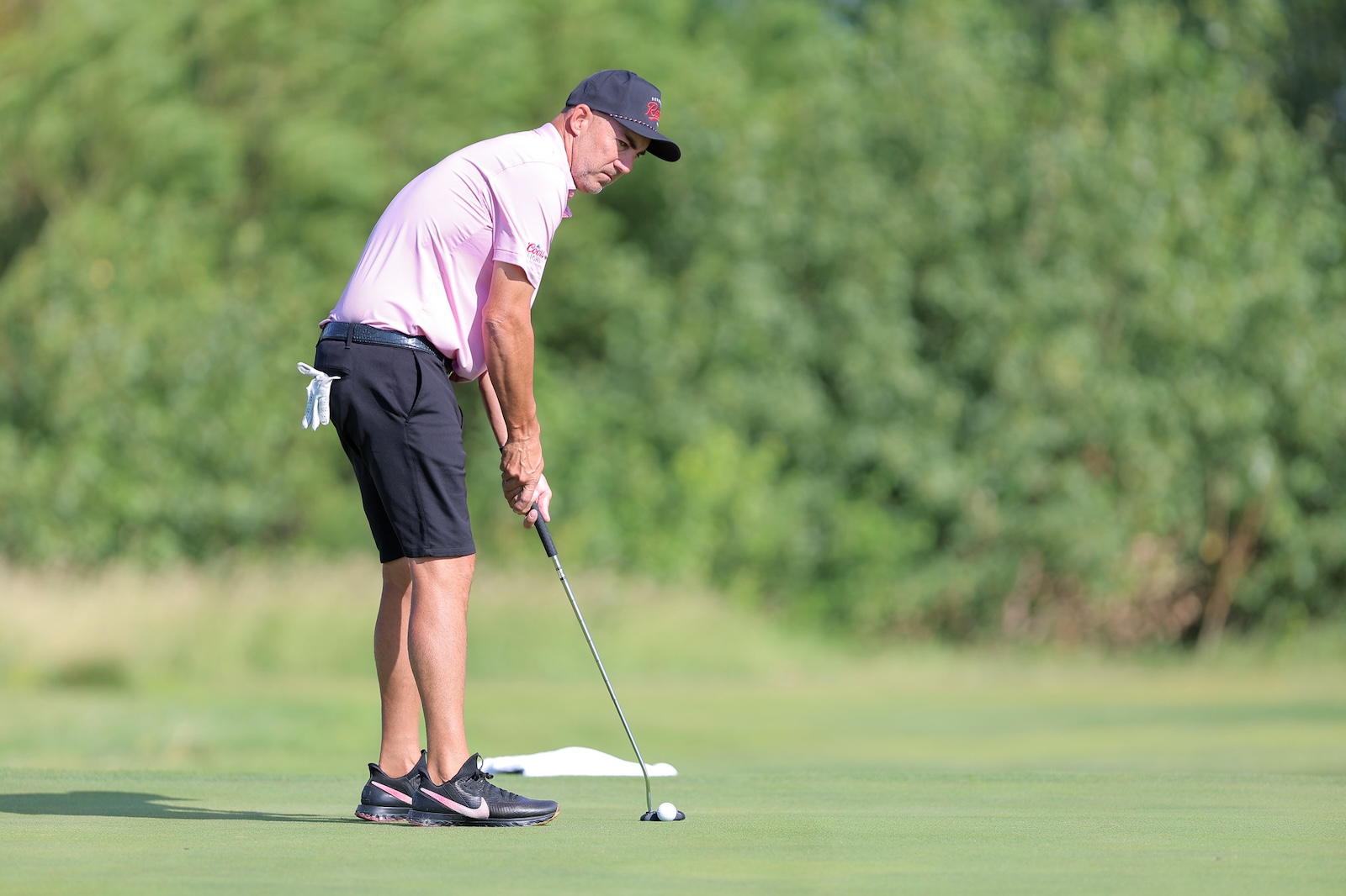 Golfer in a pink polo and black shorts lining up a putt on the green.
