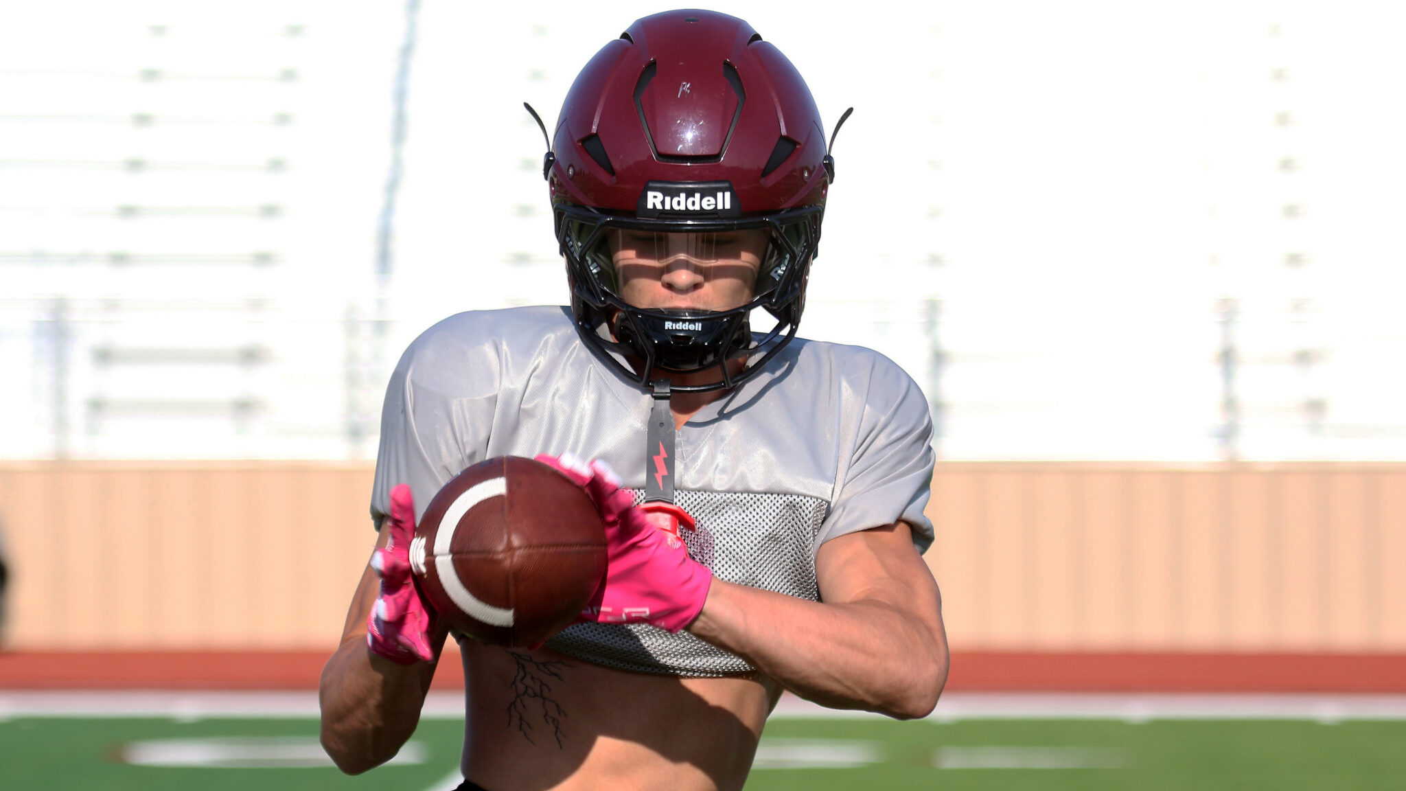1K6A5430 1 | Press Pass Sports American football player wearing a maroon helmet and gray jersey runs with a football toward the camera on a field.