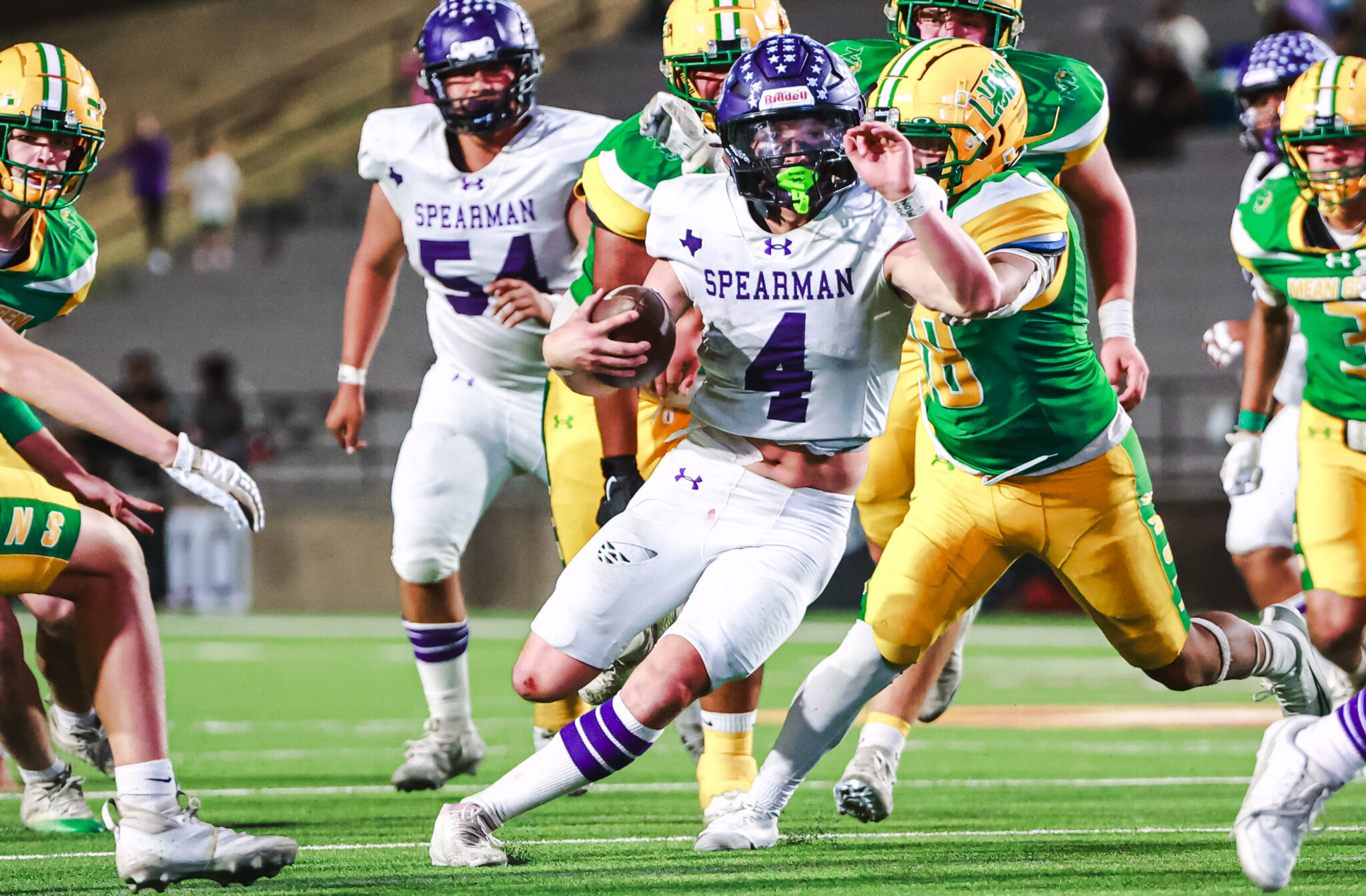 MY4A5062 1 | Press Pass Sports A Spearman player in white number 4 carries the football as defenders in green and yellow chase him on a football field.