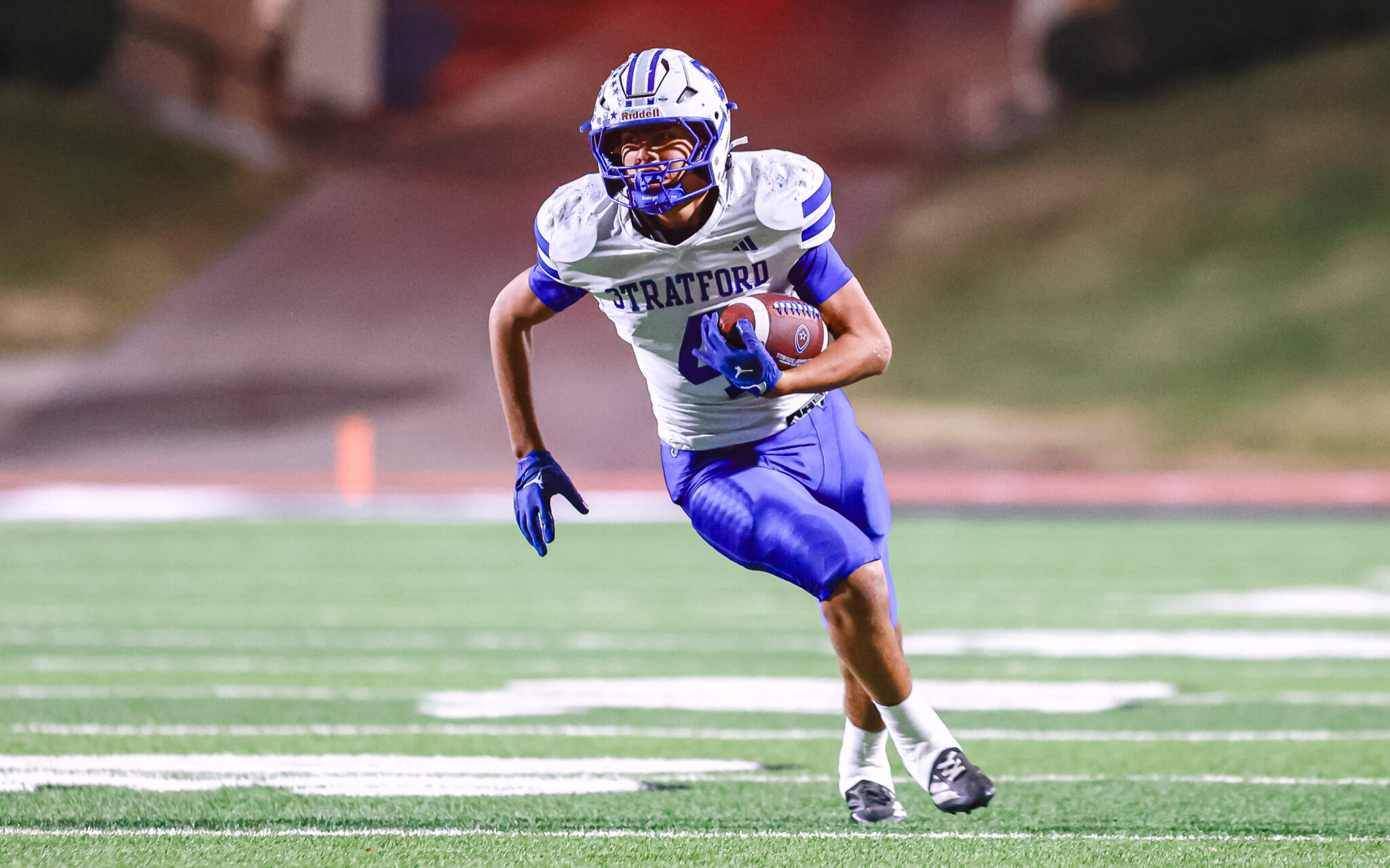 1H4A5879 | Press Pass Sports Football player in a Stratford white and blue uniform runs with a football on a green field.