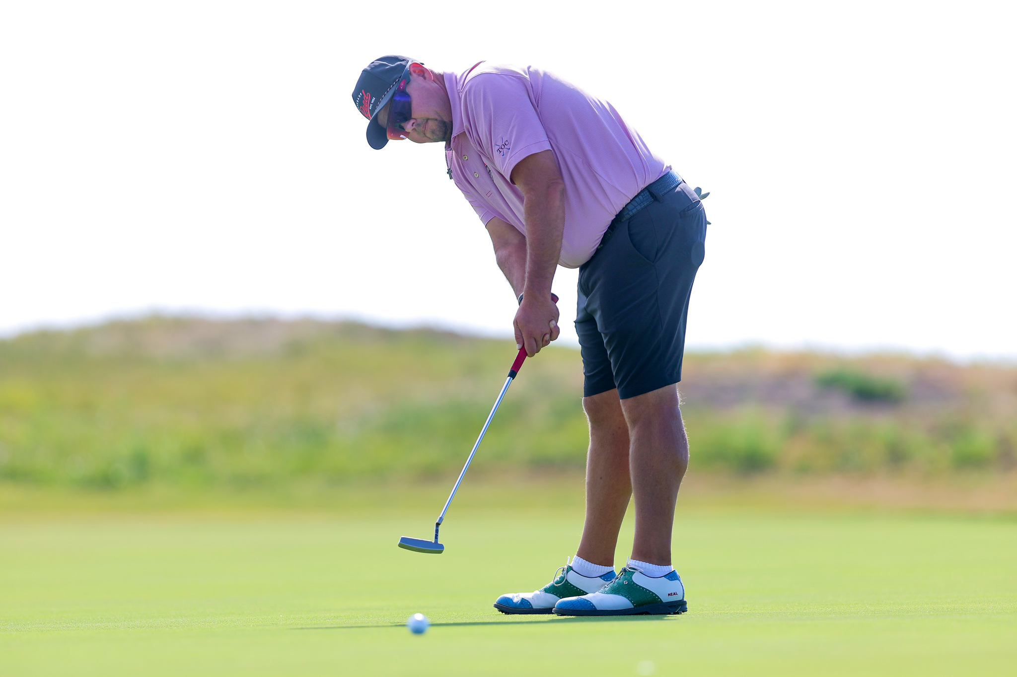 Golfer in a purple polo bending to line up a putt on a green golf course.