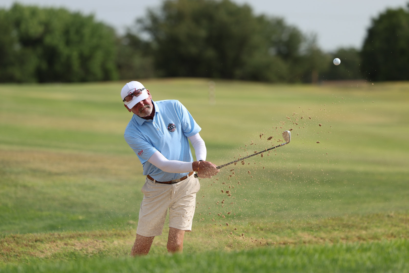 CoorTOC_FinalDay-8 | Press Pass Sports Golfer in a light blue polo and white cap mid-swing on a sunny golf course, dirt and grass spraying from the contact.