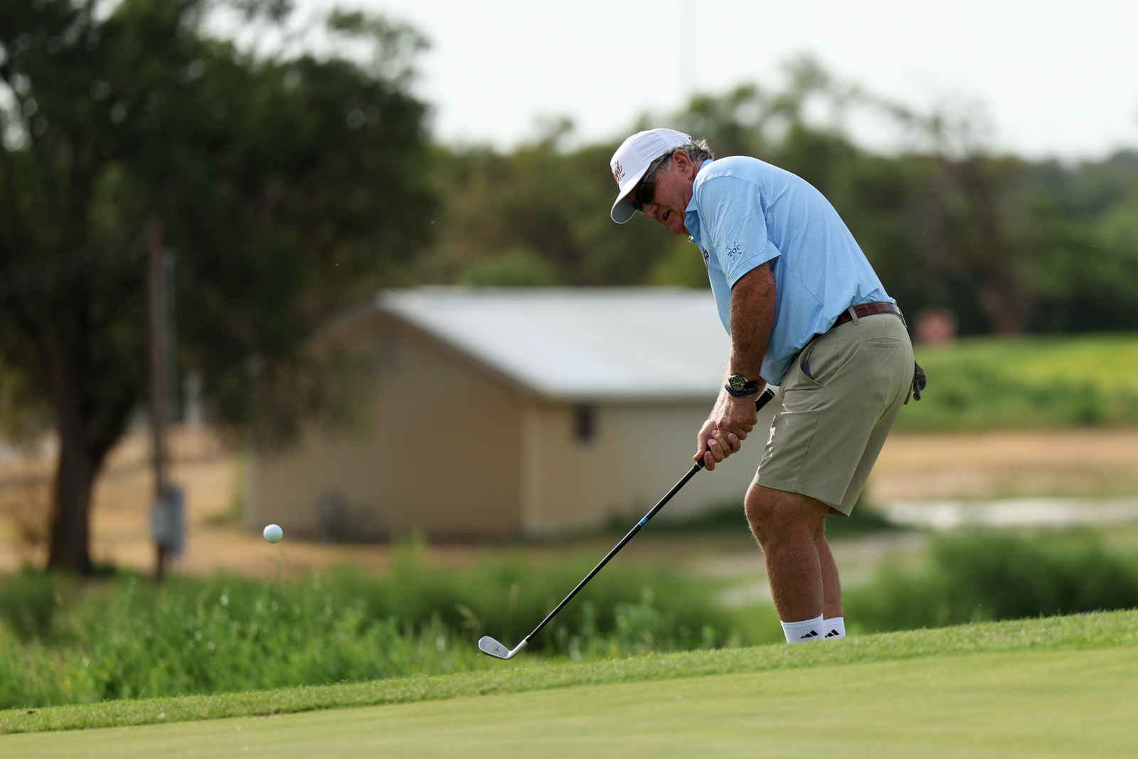 CoorTOC_FinalDay-9 | Press Pass Sports Golfer in a light blue polo and khaki shorts lining up a putt on a green fairway, wearing a white cap and sunglasses.