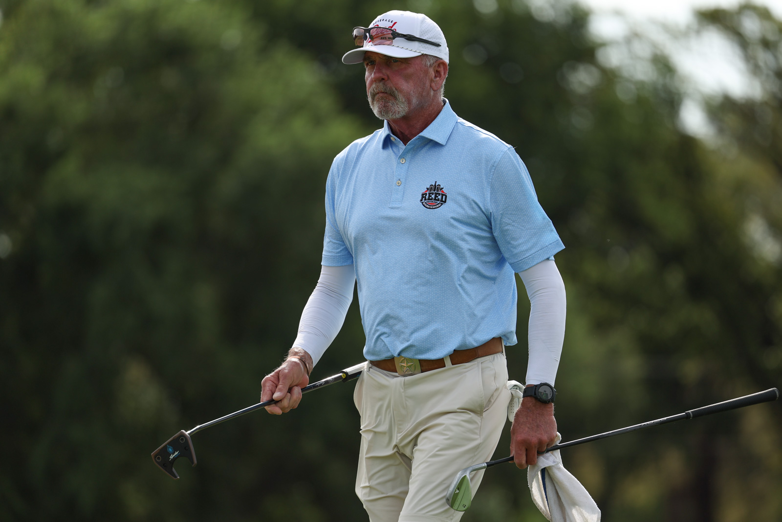 CoorTOC_FinalDay-15 | Press Pass Sports Older man in a light blue polo and white pants walks with golf clubs on a course, wearing a cap and sunglasses.