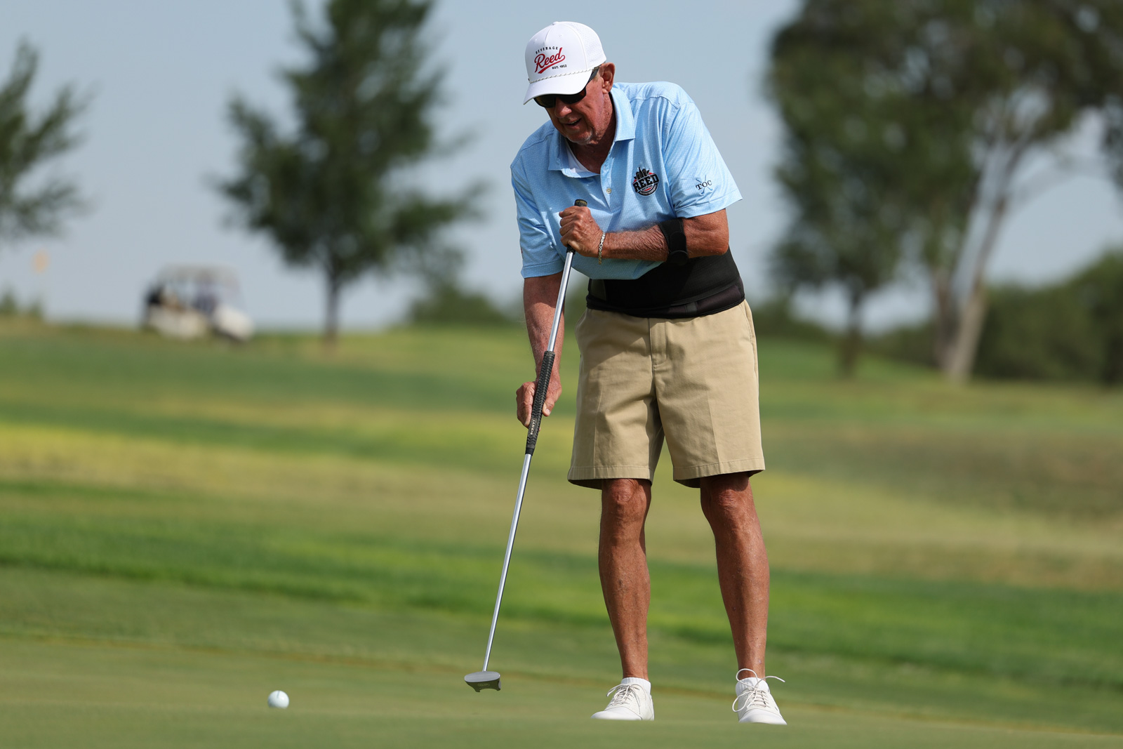 CoorTOC_FinalDay-29 | Press Pass Sports Older man in a light blue polo and white cap lining up a putt on the golf green with a putter.
