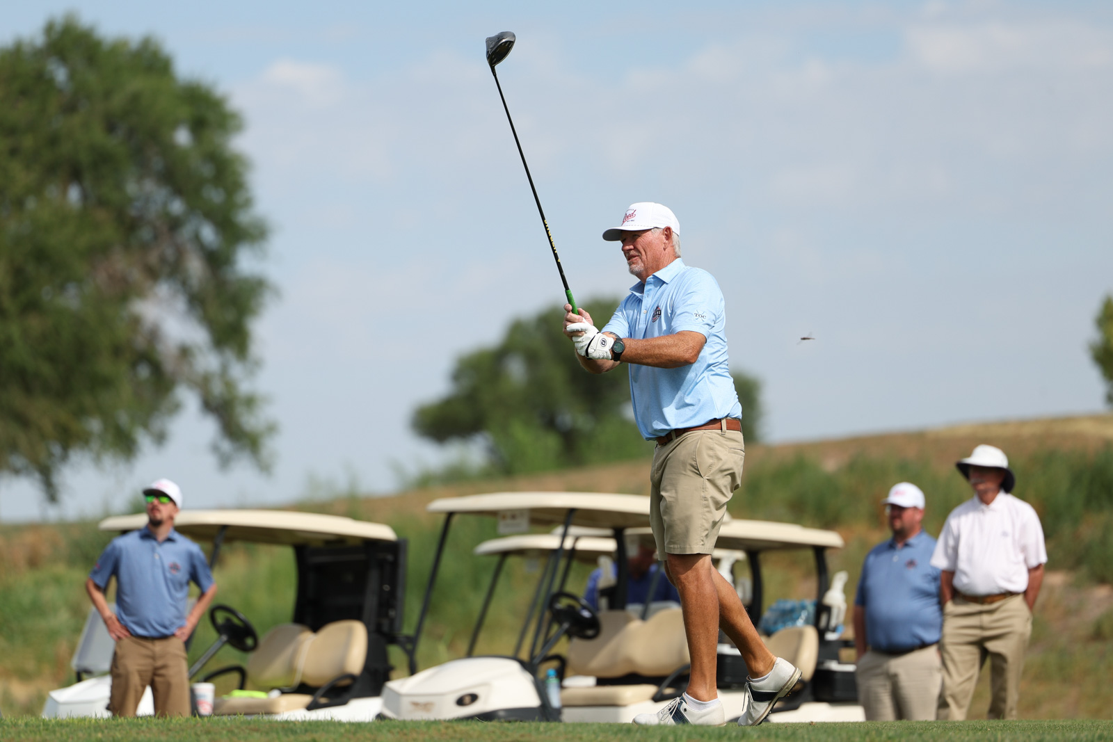 CoorTOC_FinalDay-30 | Press Pass Sports Golfer in light blue polo swings a driver on a sunny course while teammates and carts watch in the background.