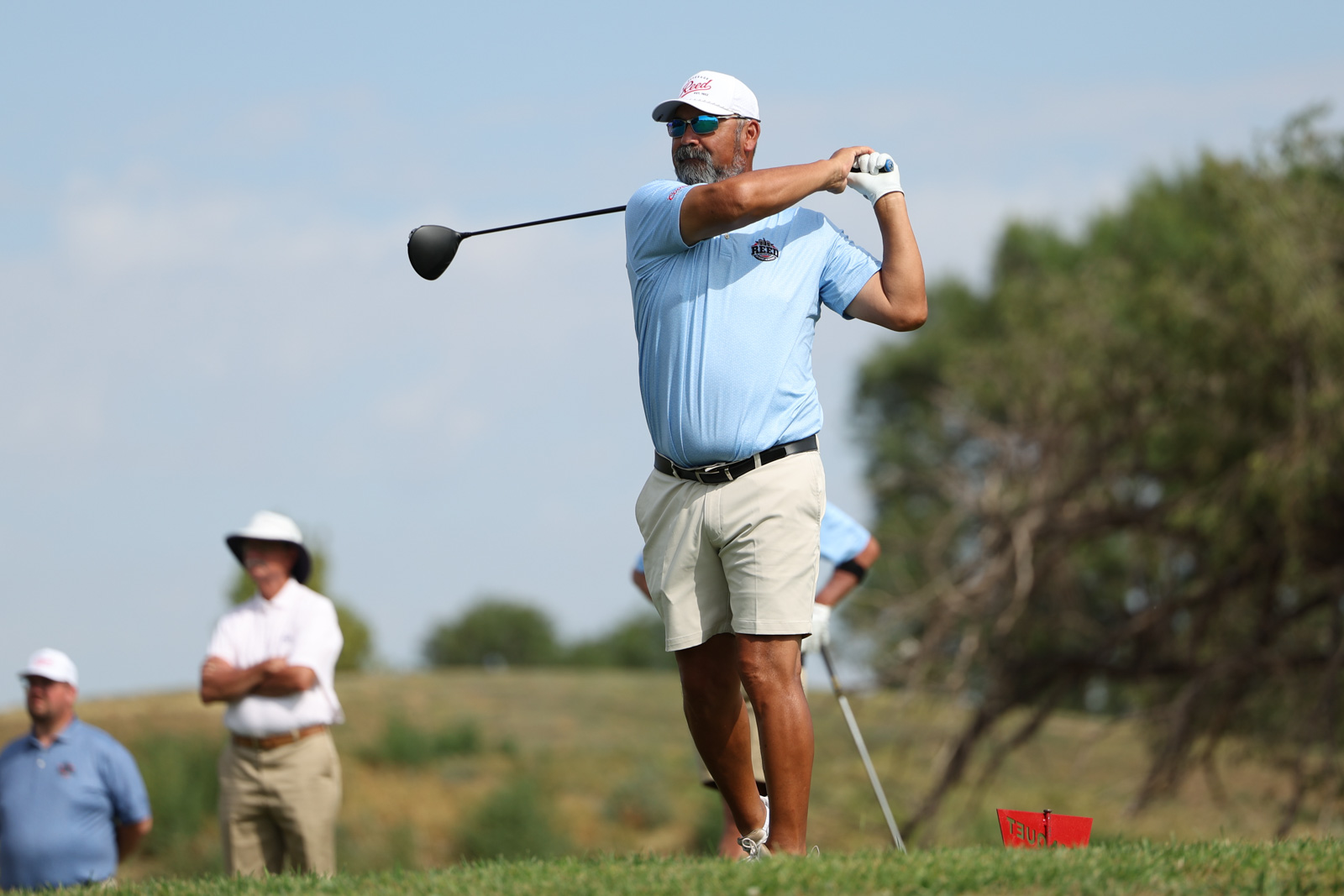 CoorTOC_FinalDay-32 | Press Pass Sports Golfer in a light blue polo and white cap mid-swing on a sunny golf course with onlookers in the background