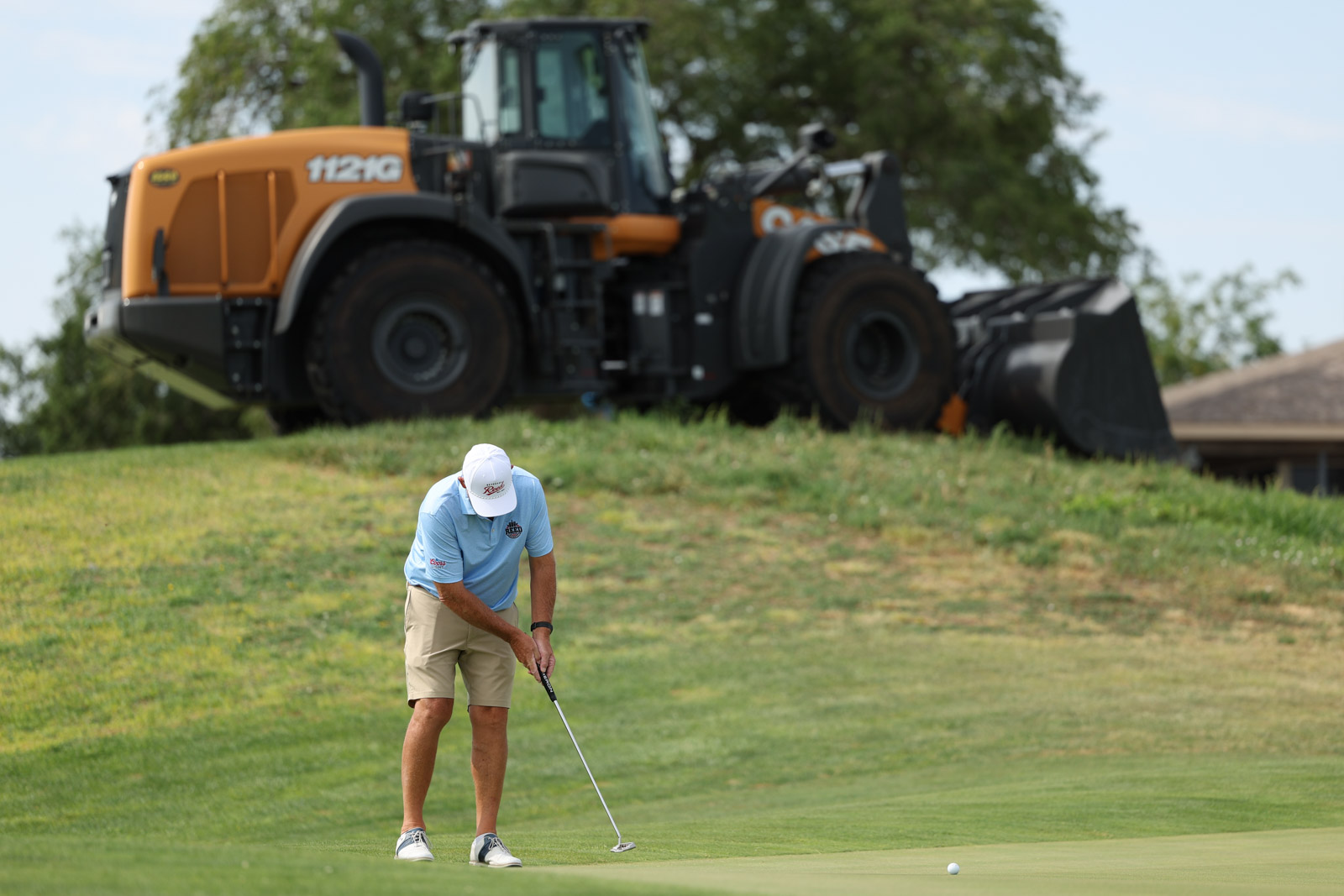 CoorTOC_FinalDay-35 | Press Pass Sports Golfer putting on a green with a large orange construction vehicle parked on a hill in the background