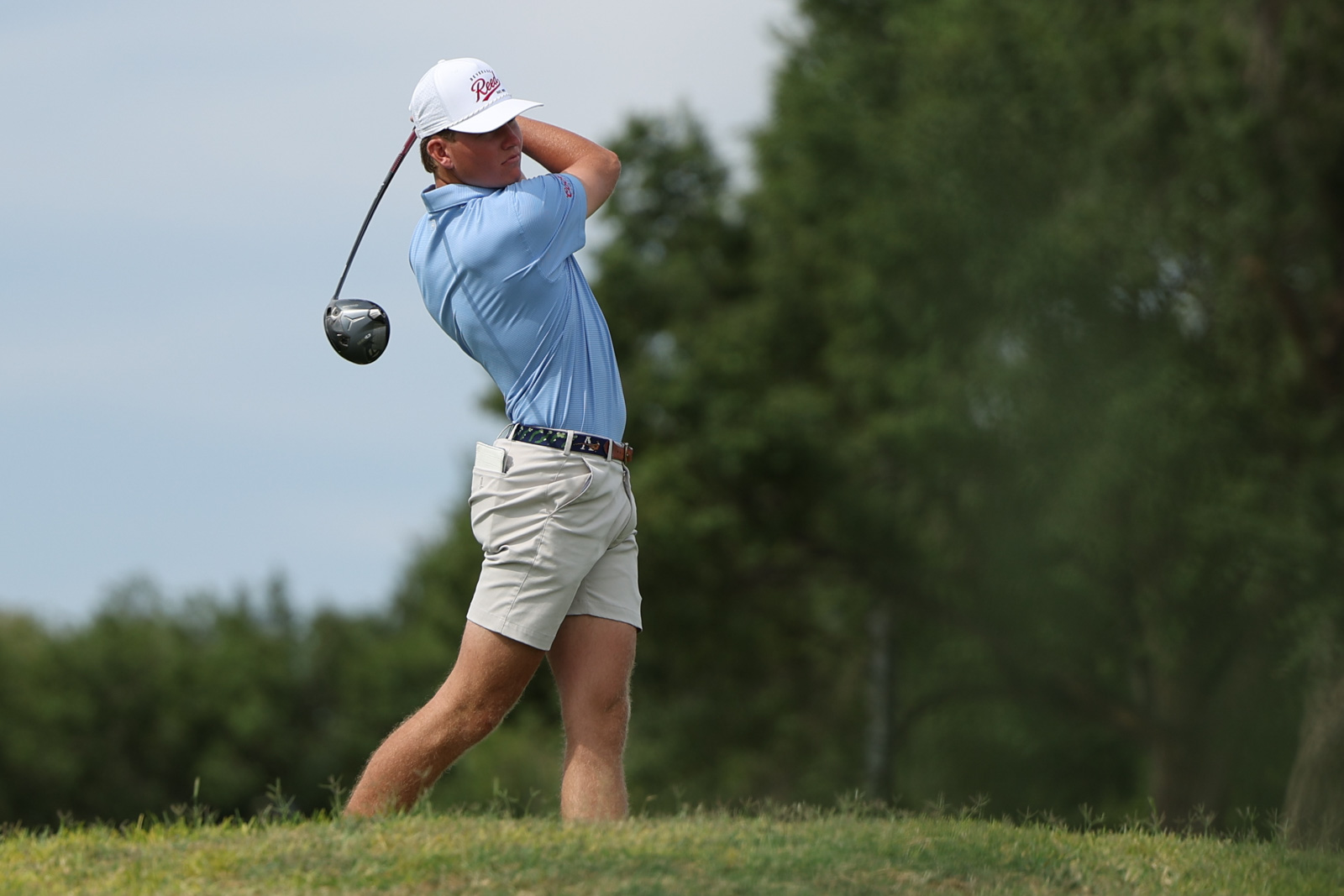 CoorTOC_FinalDay-38 | Press Pass Sports Male golfer in a light blue polo and white cap mid-swing on a grassy golf course.