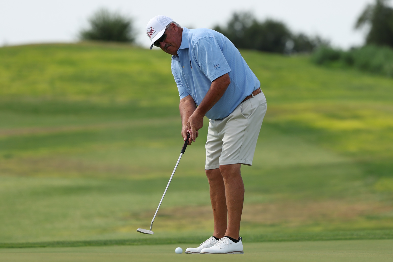 CoorTOC_FinalDay-40 | Press Pass Sports A golfer in a light blue polo lining up a putt on a green, preparing to strike a white ball toward the hole