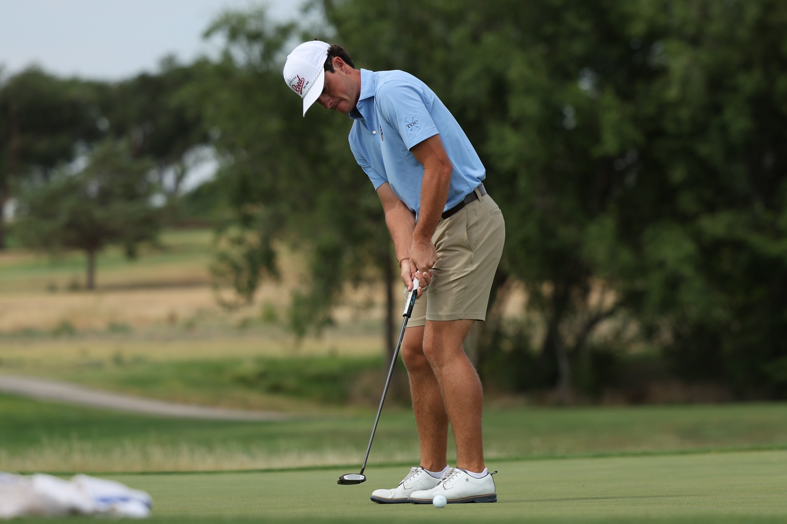 CoorTOC_FinalDay-42 | Press Pass Sports Golfer in a light blue shirt and khaki shorts lining up a putt on the green.