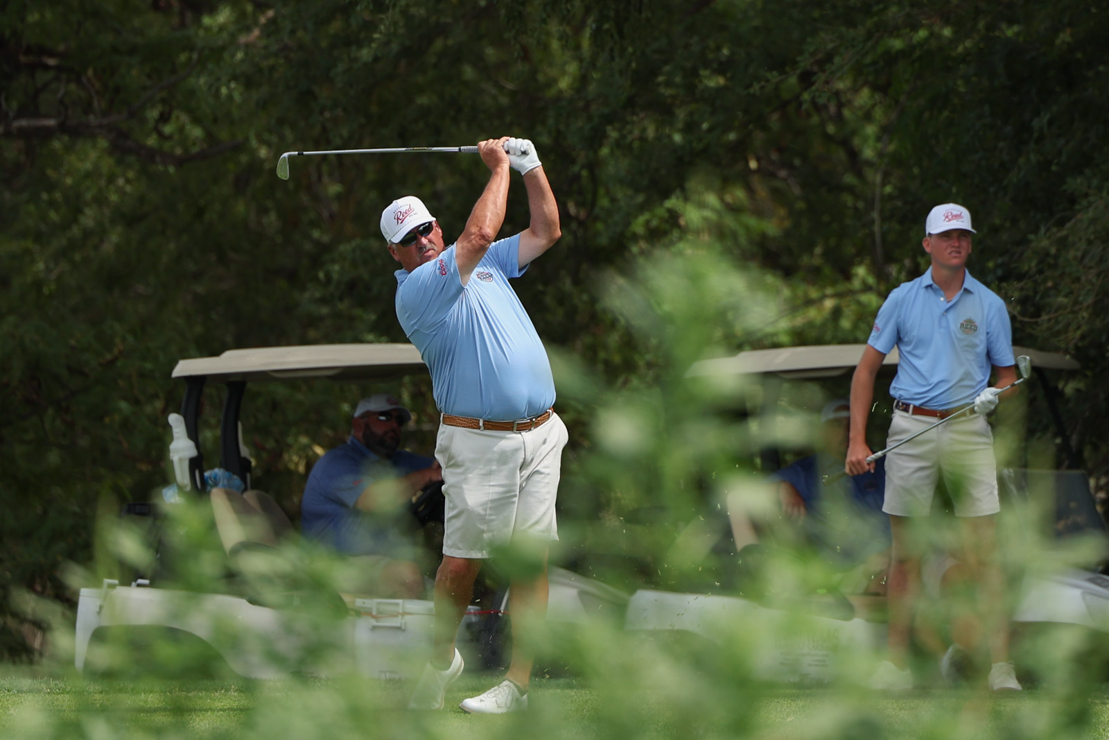 CoorTOC_FinalDay-47 | Press Pass Sports Golfer in a light blue shirt mid-swing on a sunny golf course, with a teammate watching in the background.