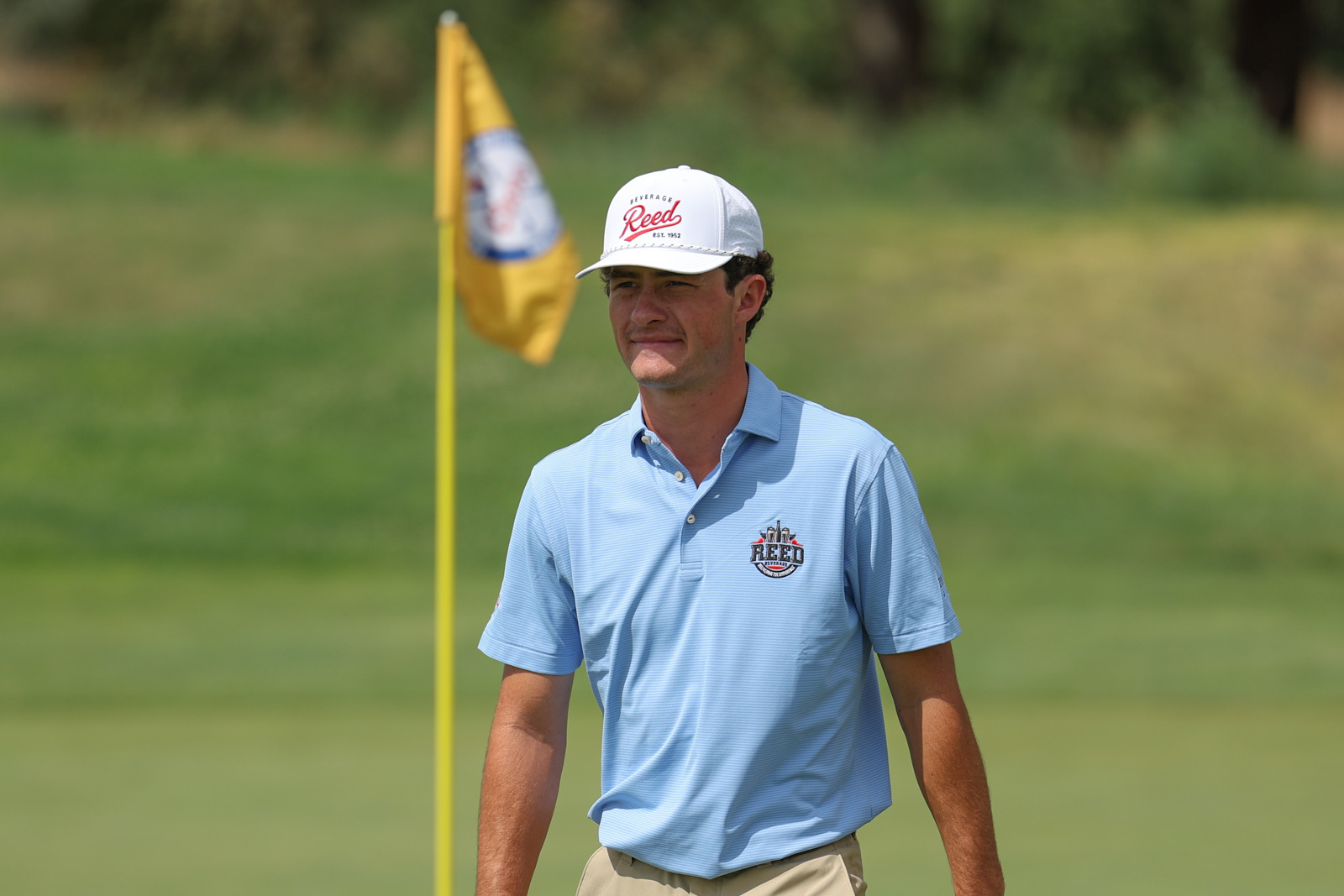 CoorTOC_FinalDay-49 | Press Pass Sports Golfer in a light blue polo shirt walking on a sunny golf course near a yellow flagstick.