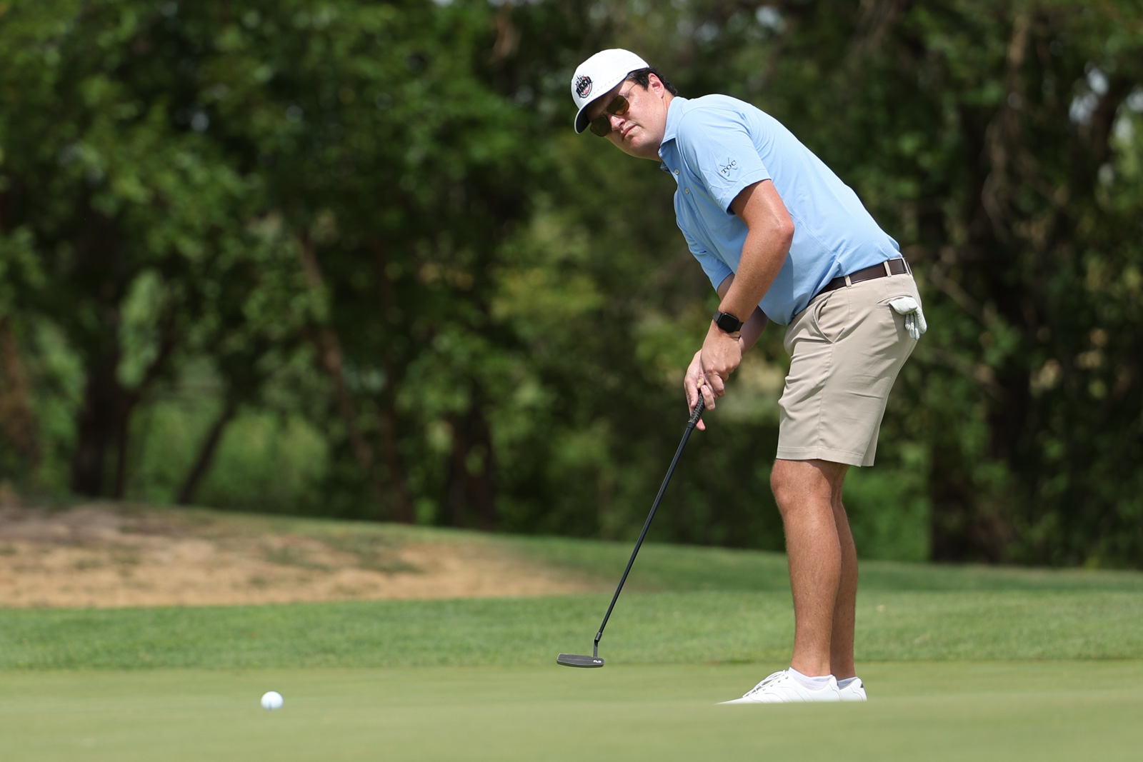 CoorTOC_FinalDay-51 | Press Pass Sports A man in a light blue polo and beige shorts putting on a golf green, wearing a white cap and sunglasses.