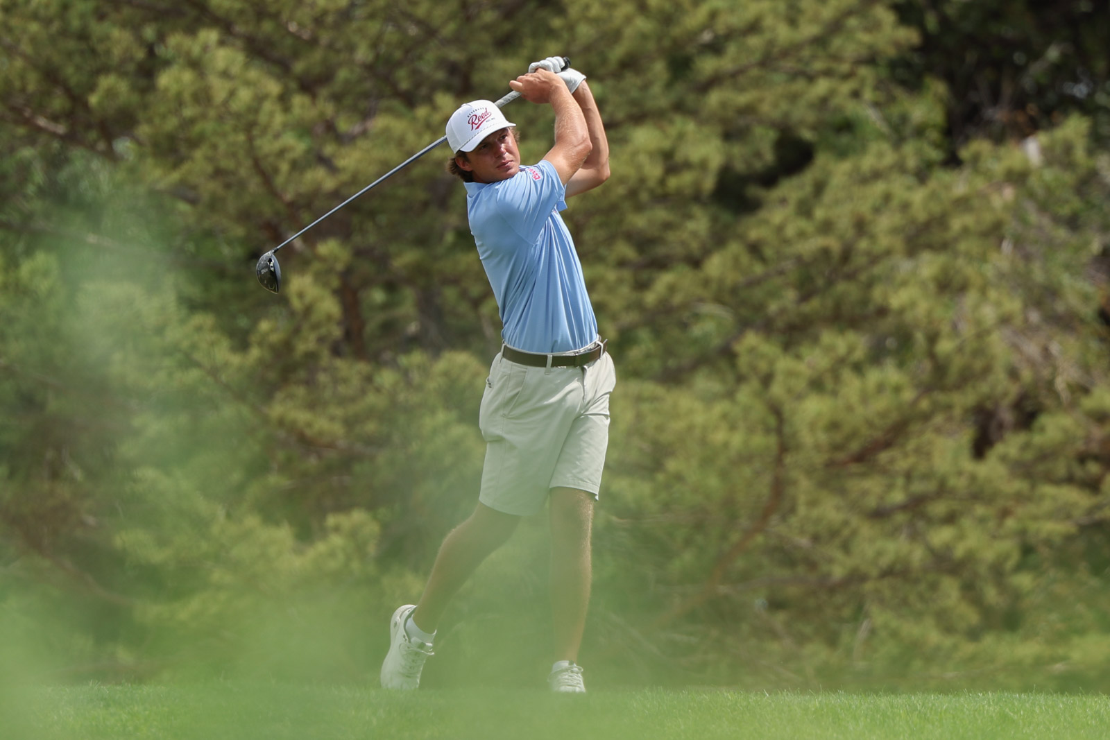 CoorTOC_FinalDay-53 | Press Pass Sports Golfer in a light blue shirt and white cap mid-swing on a green golf course with trees in the background.