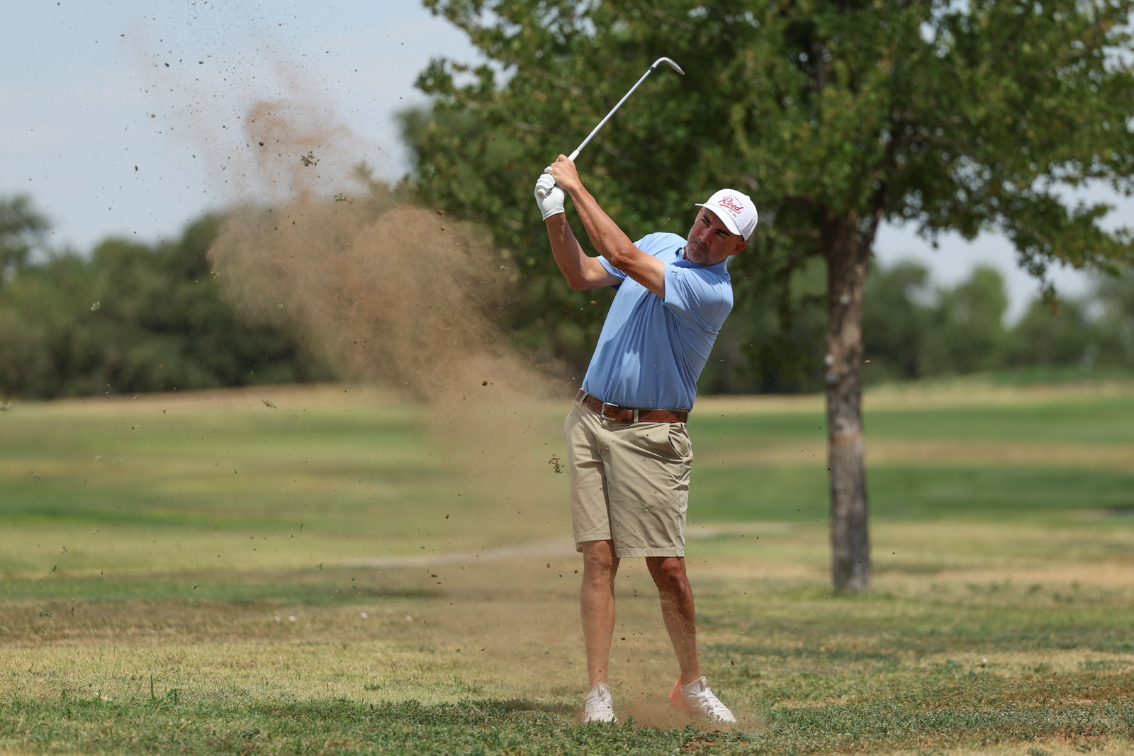 CoorTOC_FinalDay-55 | Press Pass Sports Golfer in a light blue shirt and beige shorts swings from a sand bunker, sending sand into the air.